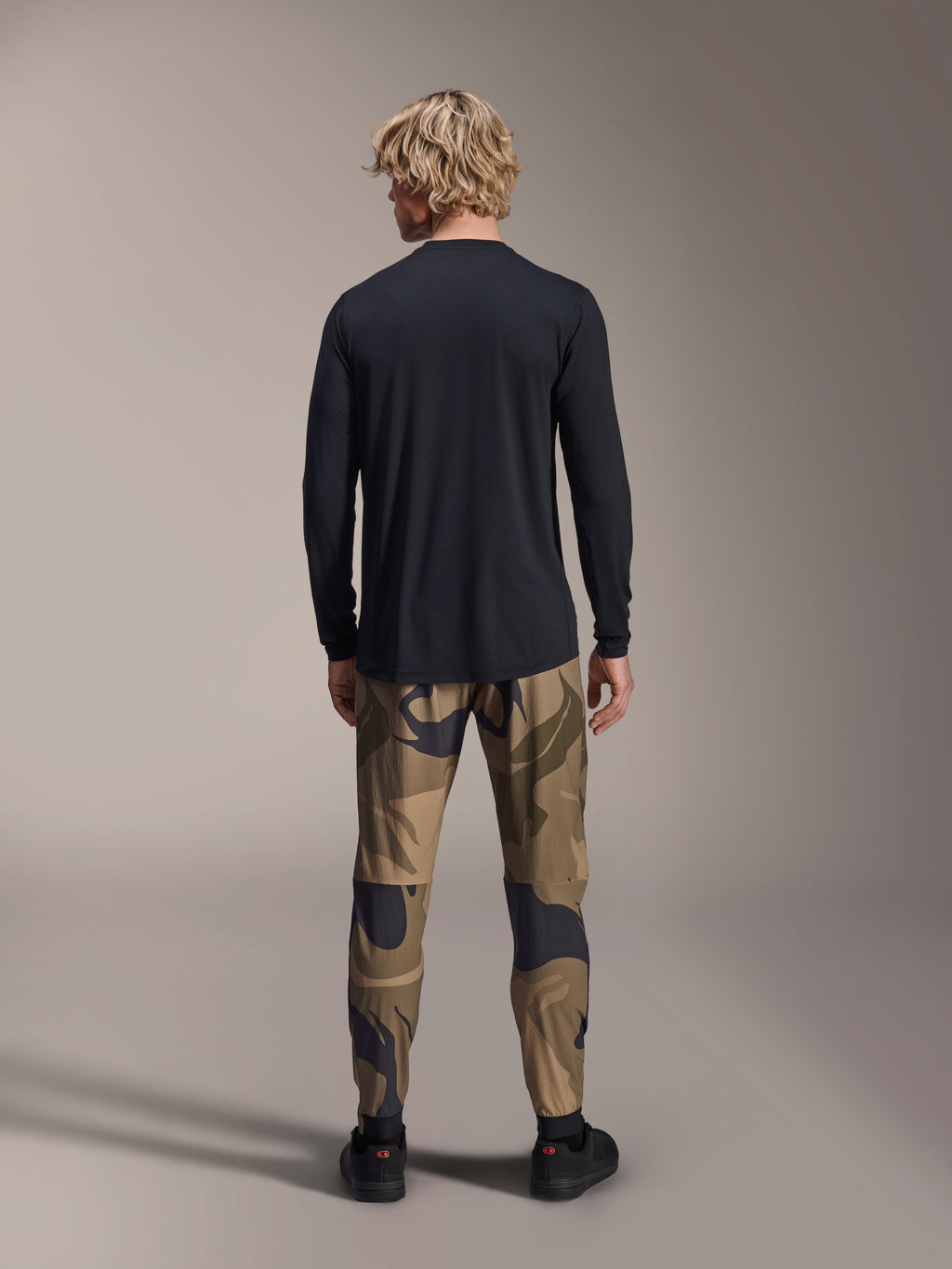 Alpinestars A-Dura Astar Långärmad Tröja, svart, vy bakifrån på modell som bär kamouflagebyxor, med förlängt ryggslut och normal passform för mountainbike