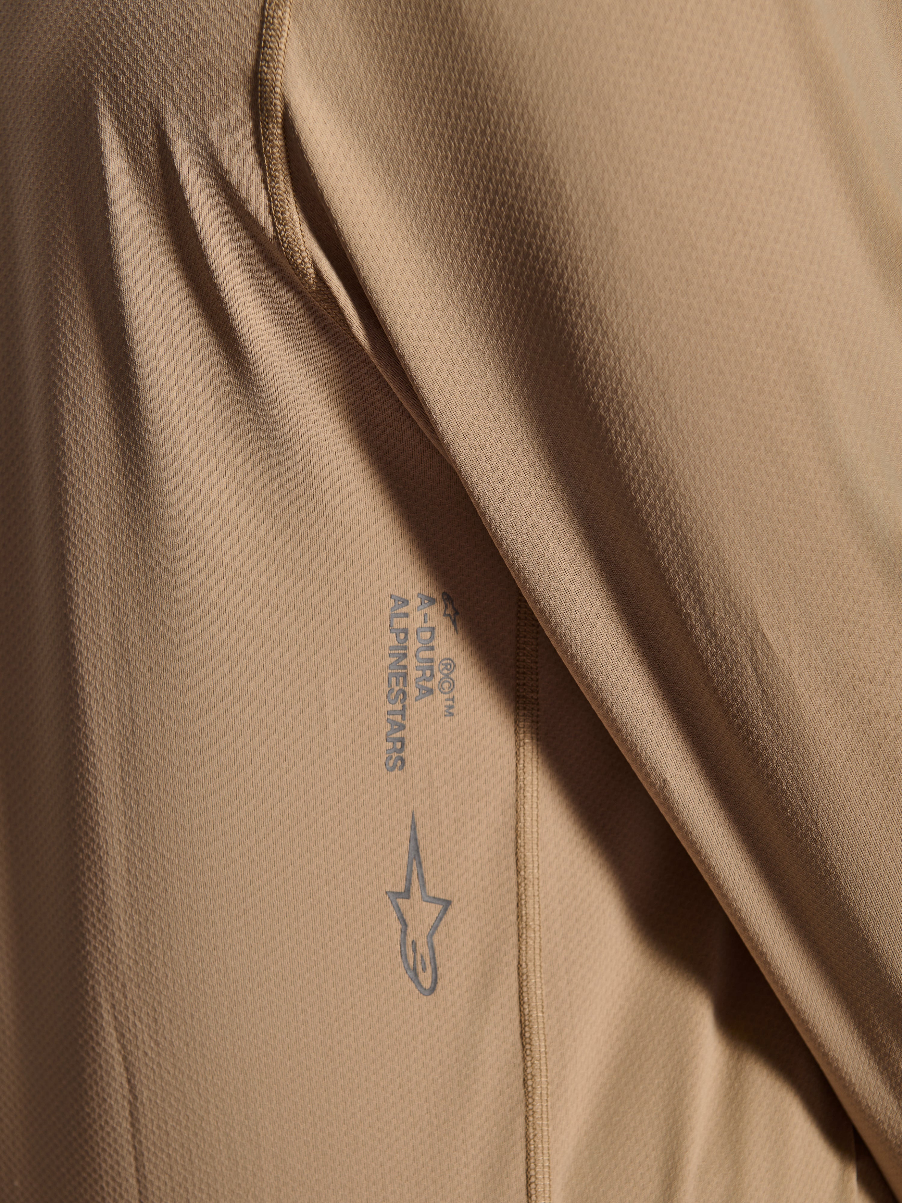 Alpinestars A-Dura Astar långärmad tröja, MTB-cykeltröja, brun, närbild som visar jacquard-tygets struktur, tryckt Astars-logotyp och A-Dura-ordmärke, teknisk mountainbike-utrustning