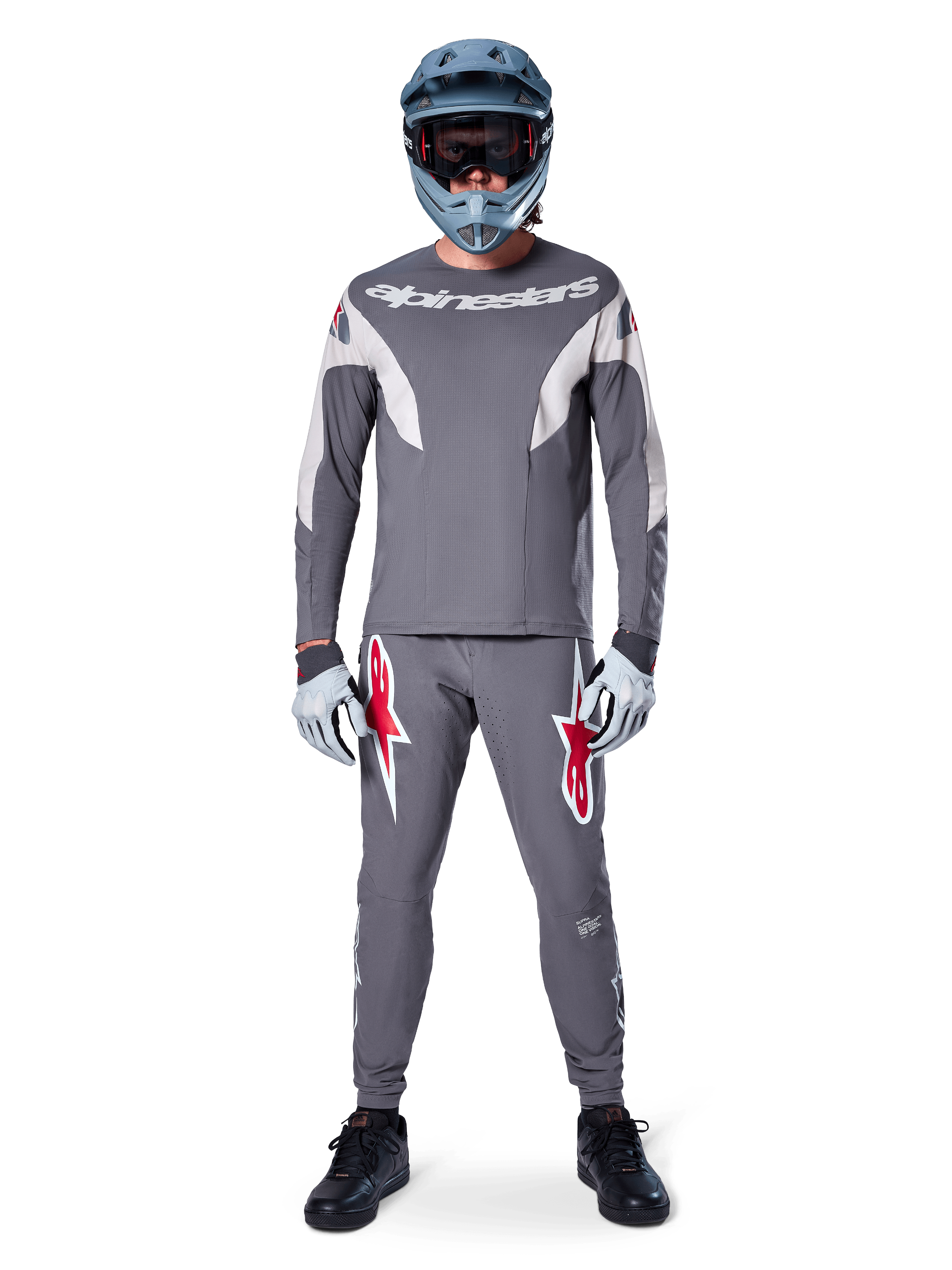 Rider wearing the Alpinestars A-Supra Race Jersey - Long Sleeve in Dark Gray, coordinated with matching gray pants featuring bold red star logos, gray helmet with goggles, and light gray gloves, complete MTB racing kit for performance off-road cycling