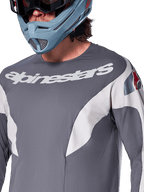 Alpinestars A-Supra Race Jersey - Long Sleeve, MTB Jersey, Dark Gray with white racing graphics and white Alpinestars logo, worn with a light blue full-face helmet and goggles, micro-perforated fabric for off-road performance