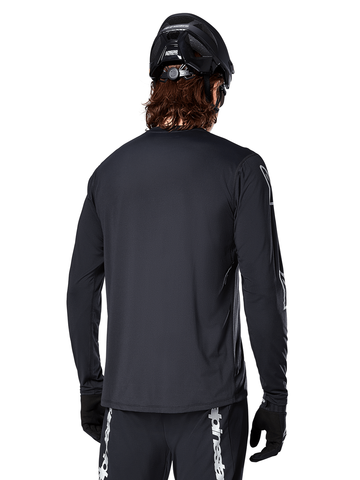 Alpinestars A-Dura Switch långärmad tröja, svart, vy bakifrån på en cyklist med svart MTB-hjälm och handskar, med tekniskt jacquardvävt tyg och förlängt bakstycke för terrängkörning