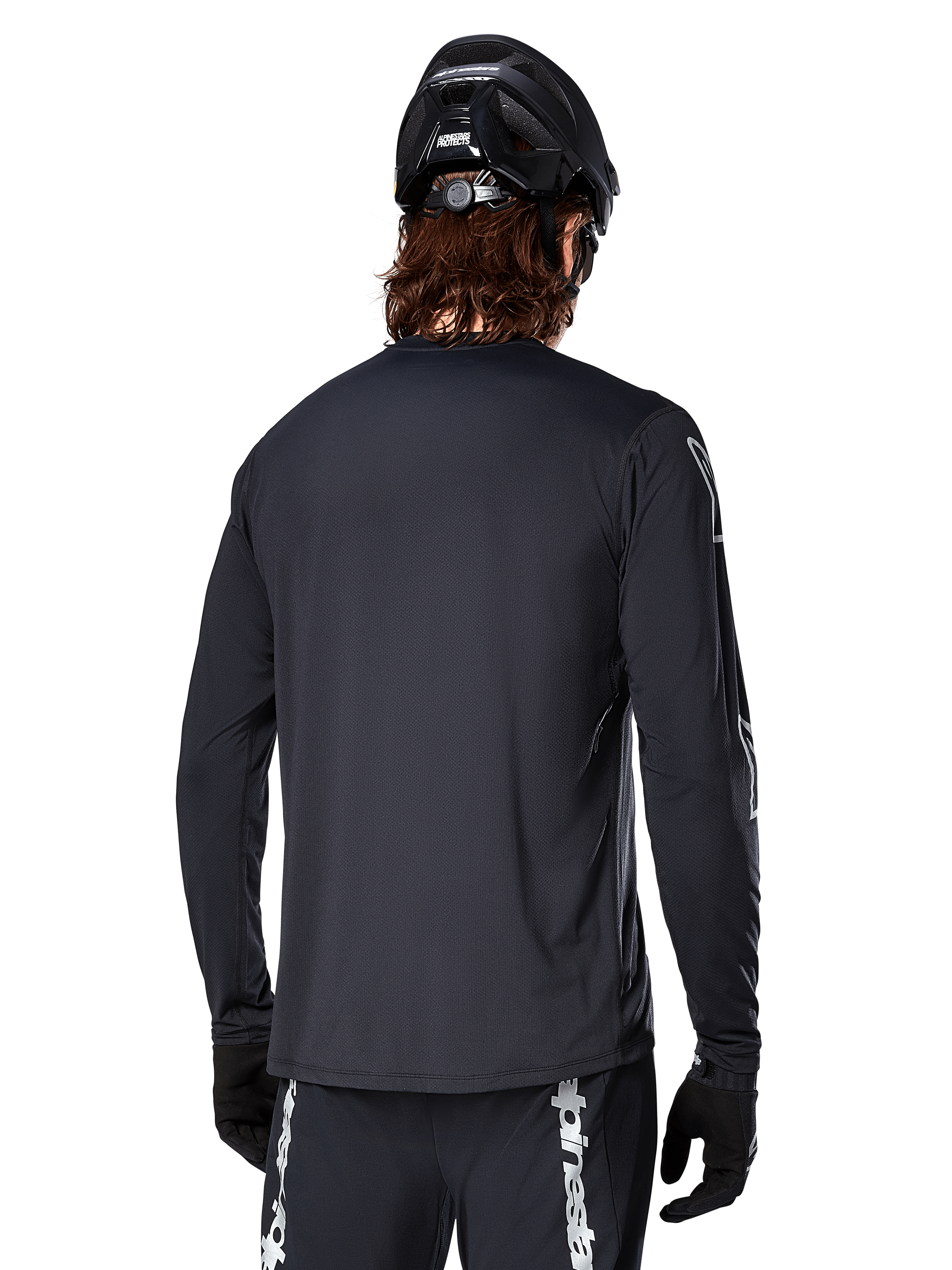 Alpinestars A-Dura Switch långärmad tröja, svart, vy bakifrån på en cyklist med svart MTB-hjälm och handskar, med tekniskt jacquardvävt tyg och förlängt bakstycke för terrängkörning