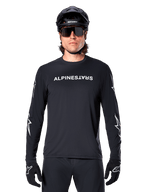Alpinestars A-Dura Switch långärmad tröja, svart MTB-tröja, vit Alpinestars-ordmärkeslogotyp på bröstet och stjärngrafik på ärmarna, bärs med svart mountainbikehjälm och sportglasögon, tekniska kläder för stigcykling