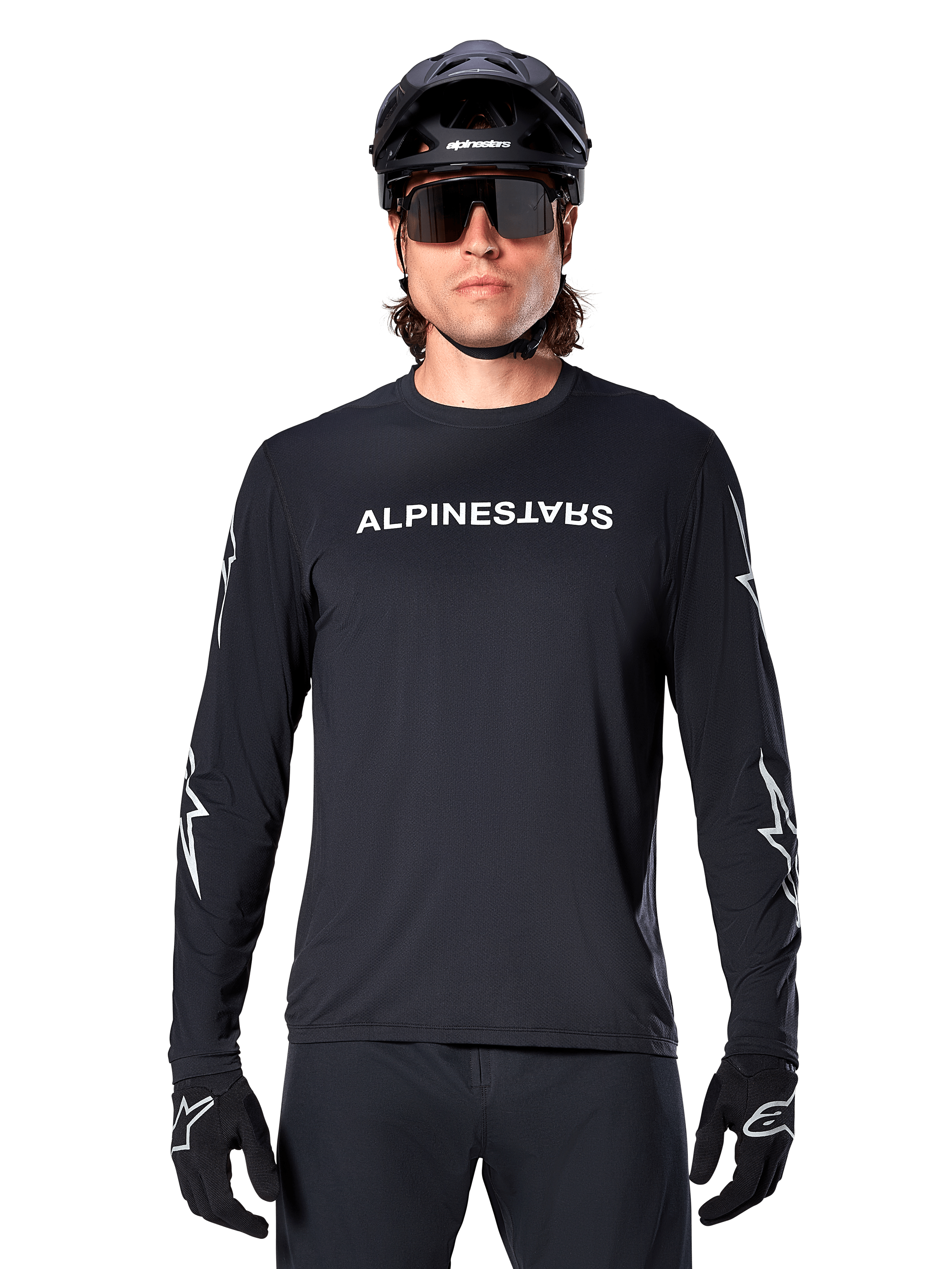 Alpinestars A-Dura Switch långärmad tröja, svart MTB-tröja, vit Alpinestars-ordmärkeslogotyp på bröstet och stjärngrafik på ärmarna, bärs med svart mountainbikehjälm och sportglasögon, tekniska kläder för stigcykling
