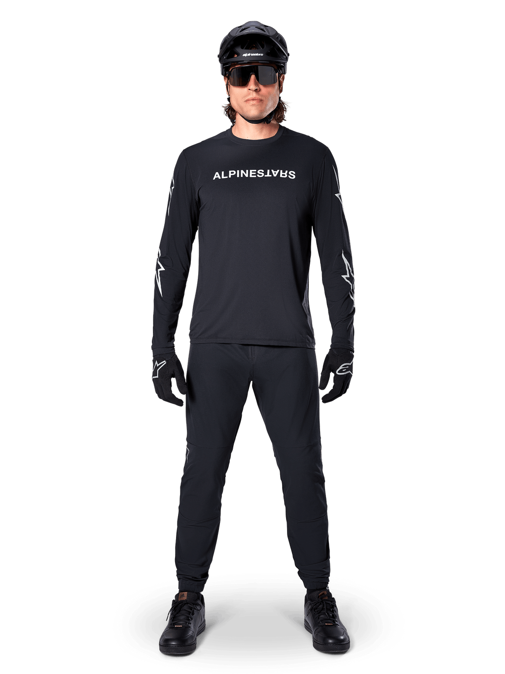 Alpinestars A-Dura Switch långärmad tröja, svart, bärs av en mountainbikecyklist med matchande svarta byxor och hjälm, vit ordmärkeslogotyp på bröstet, tekniska cykelkläder för terrängkörning