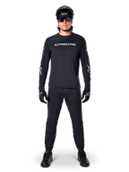 Alpinestars A-Dura Switch långärmad tröja, svart, bärs av en mountainbikecyklist med matchande svarta byxor och hjälm, vit ordmärkeslogotyp på bröstet, tekniska cykelkläder för terrängkörning