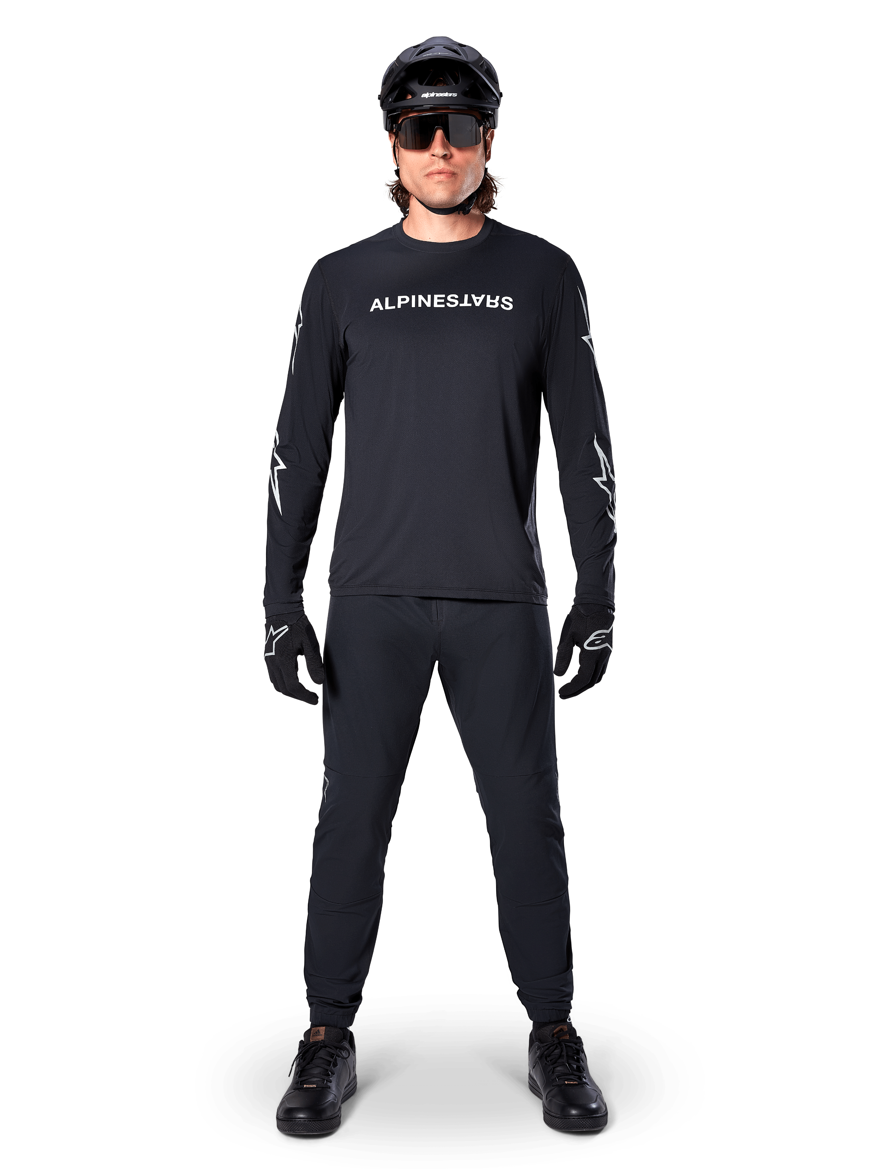 Alpinestars A-Dura Switch långärmad tröja, svart, bärs av en mountainbikecyklist med matchande svarta byxor och hjälm, vit ordmärkeslogotyp på bröstet, tekniska cykelkläder för terrängkörning