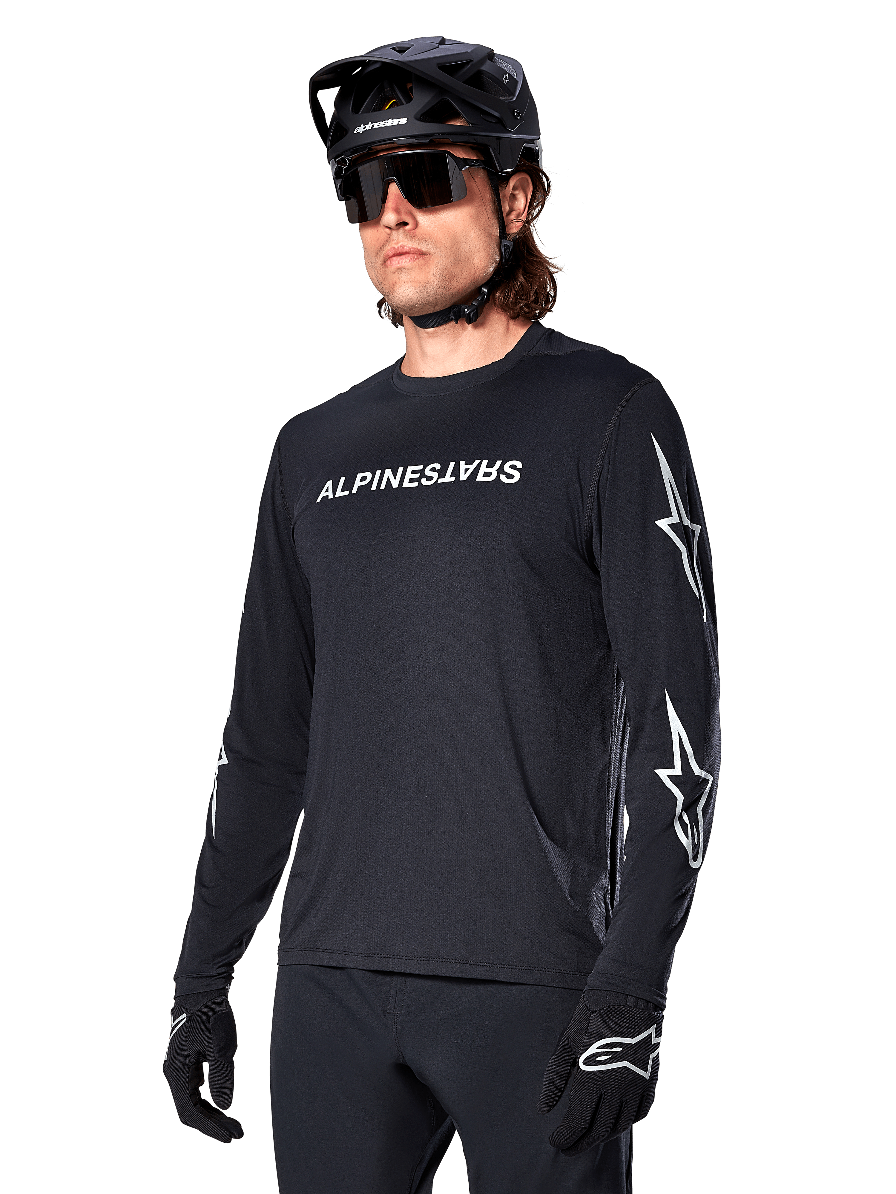 Manlig cyklist i Alpinestars A-Dura Switch långärmad tröja, svart med vit ordmärkeslogotyp och stjärnlogotyper på ärmarna, kombinerad med svart MTB-hjälm och solglasögon, högpresterande cykelutrustning för terrängcykling