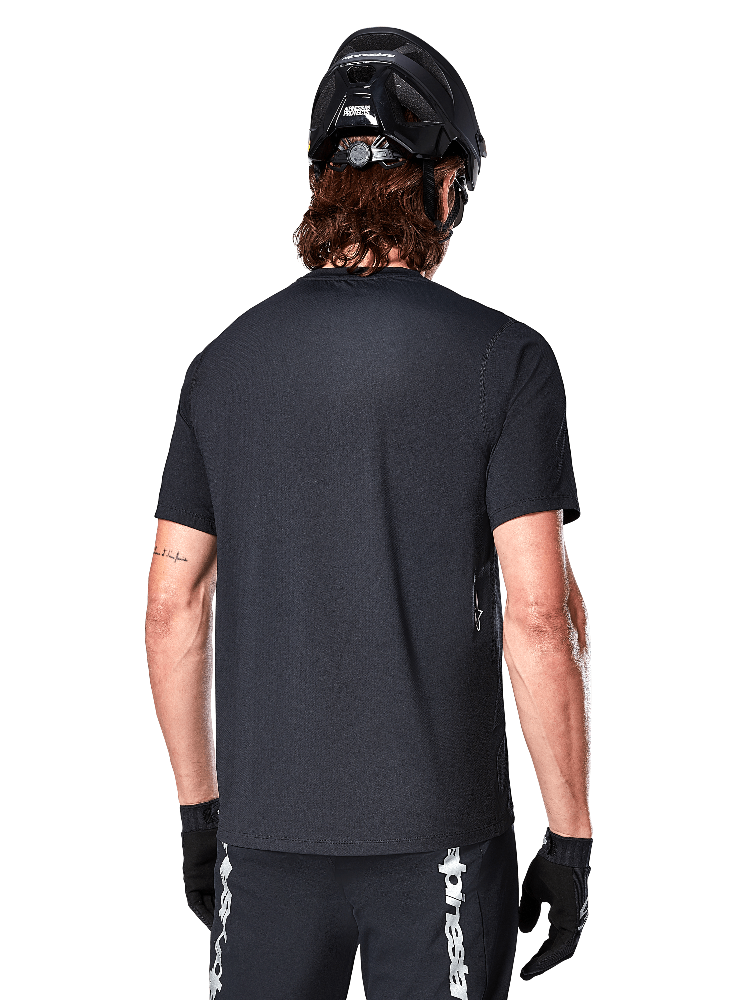 Alpinestars A-Dura Switch kortärmad tröja, svart, vy bakifrån på en modell med svart cykelhjälm och MTB-shorts, framhäver den normala passformen och den förlängda ryggen för mountainbike.