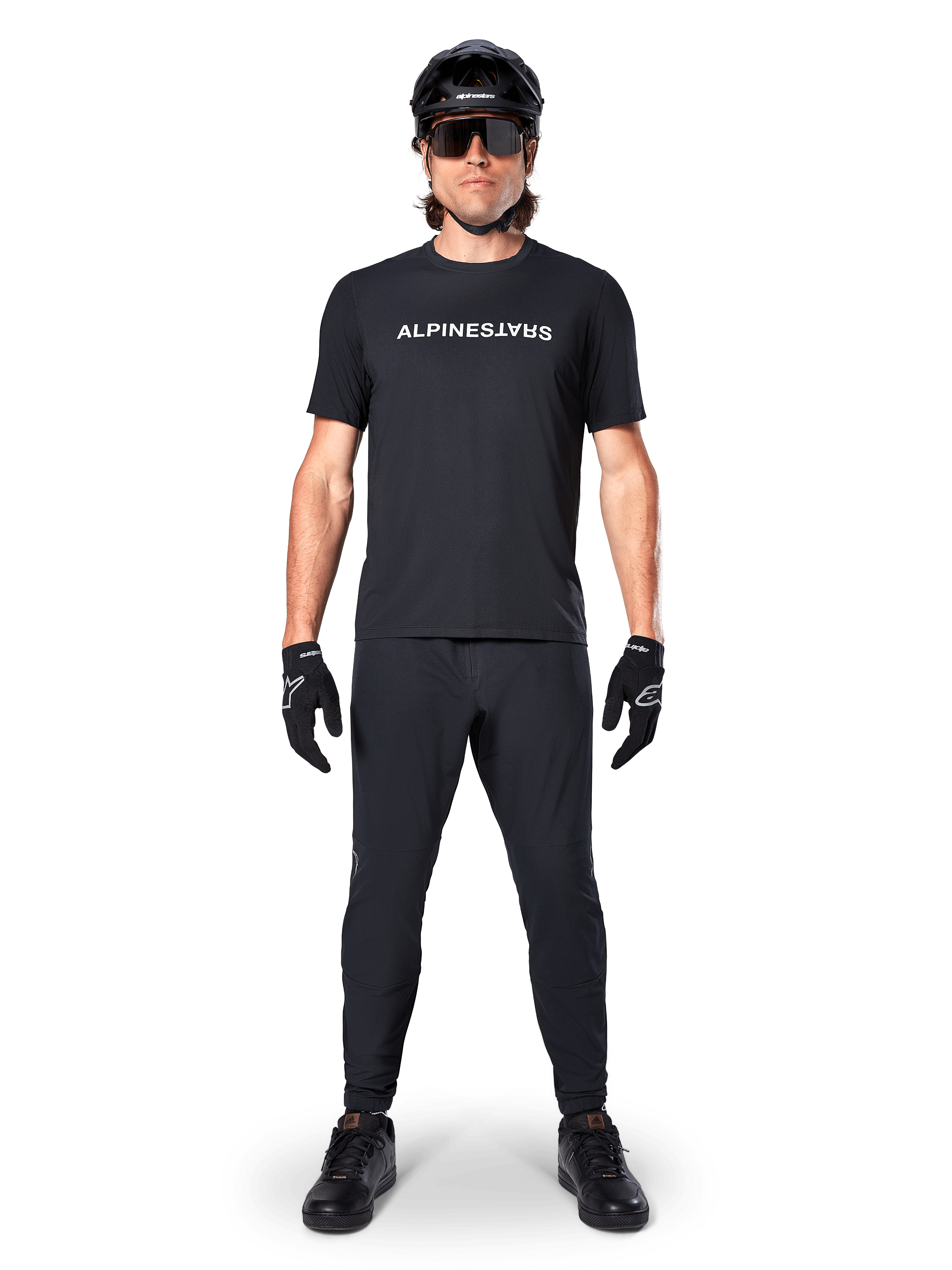 Mountainbike-cyklist i Alpinestars A-Dura Switch kortärmad tröja i svart, med vit stiliserad logotyp på bröstet, matchat med svarta MTB-byxor, hjälm och handskar, komplett cykeloutfit för stigcykling.