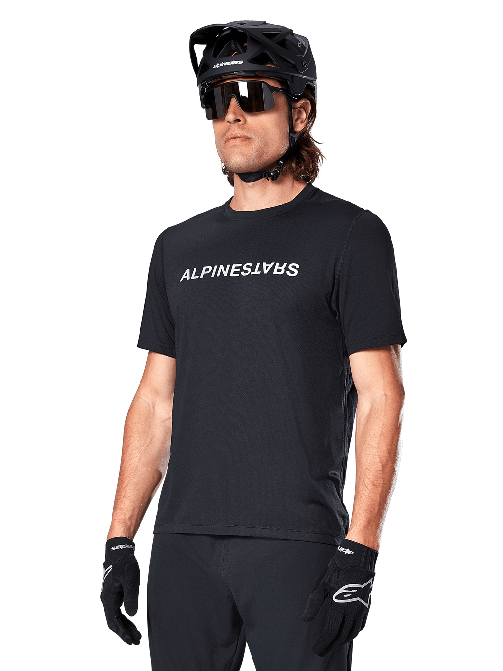 Alpinestars A-Dura Switch kortärmad tröja, svart, med en vit ordmärkeslogotyp på bröstet, bärs av en cyklist med svart MTB-hjälm och solglasögon, tekniska kläder designade för stigcykling