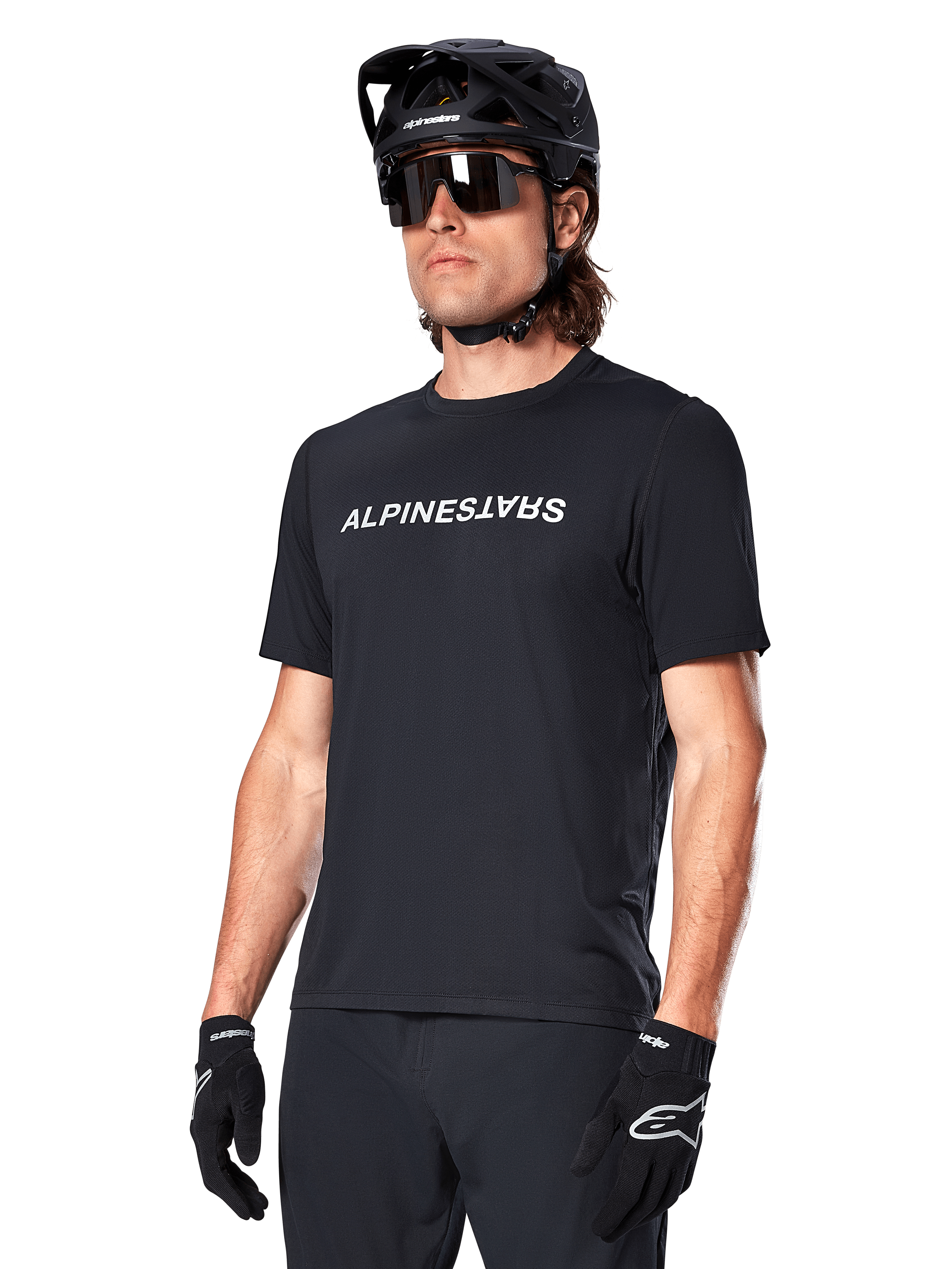 Alpinestars A-Dura Switch kortärmad tröja, svart, med en vit ordmärkeslogotyp på bröstet, bärs av en cyklist med svart MTB-hjälm och solglasögon, tekniska kläder designade för stigcykling