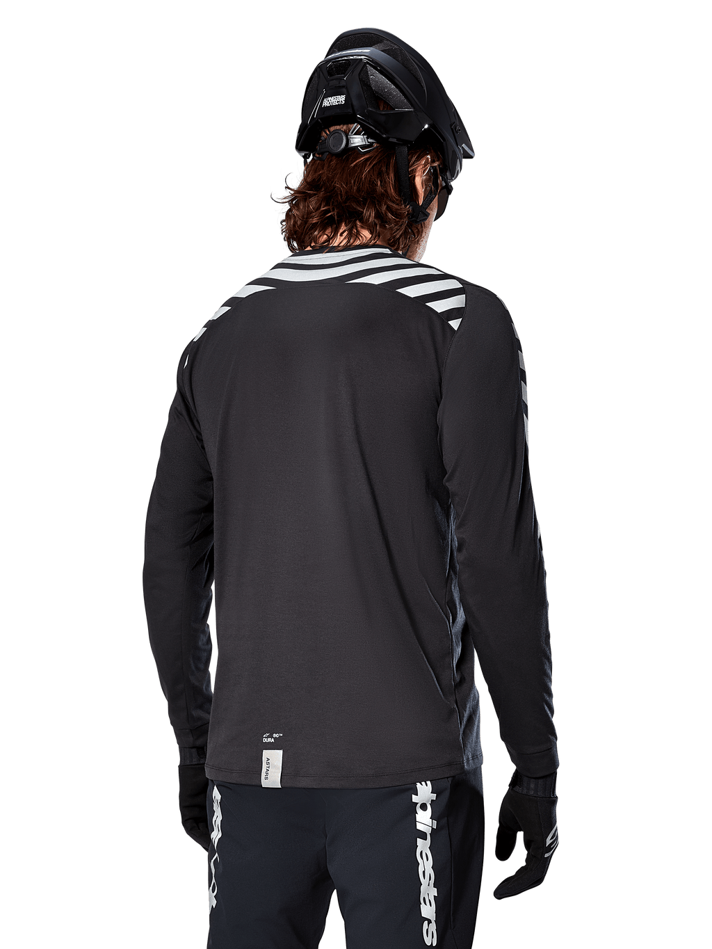 Alpinestars A-Dura Dri Oscar långärmad tröja, Black Reflective, vy bakifrån som visar reflekterande diagonala ränder på axlarna och ett förlängt ryggslut, buren med svart MTB-hjälm och handskar, teknisk utrustning för mountainbike