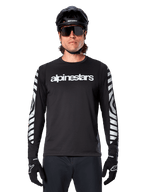 Manlig cyklist i Alpinestars A-Dura Dri Oscar långärmad tröja, Black Reflective, med vit Alpinestars-text på bröstet och reflekterande silvergrafik på ärmarna, kombinerat med svart MTB-hjälm, solglasögon och svarta handskar, teknisk cykelutrustning