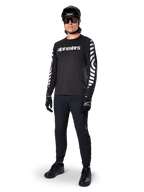 Alpinestars A-Dura Dri Oscar långärmad tröja, Black Reflective, med en tydlig vit Alpinestars-textlogotyp på bröstet och reflekterande grafiska mönster på ärmarna, bärs med svarta mountainbikebyxor, hjälm och handskar, tekniska MTB-kläder
