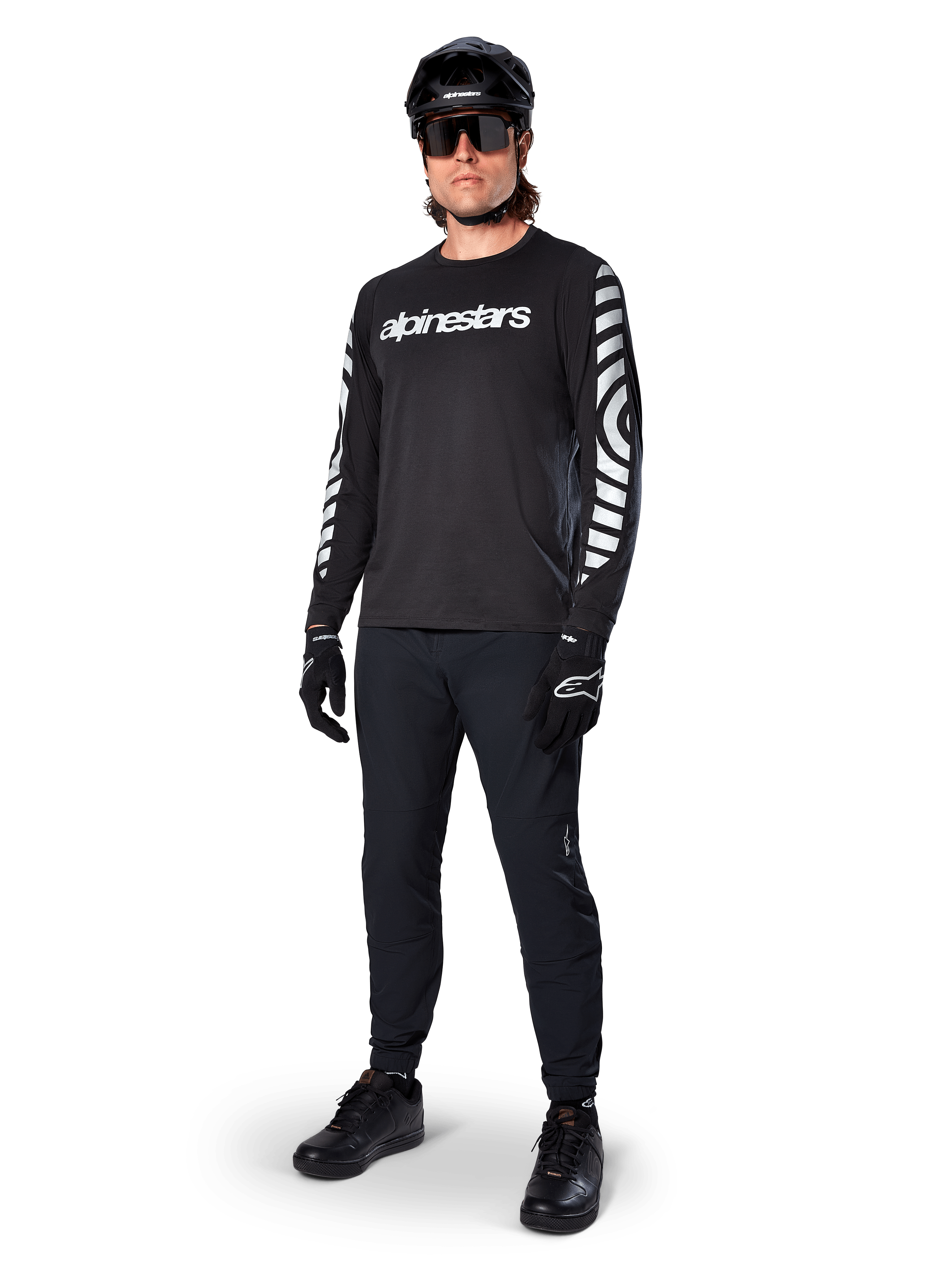 Alpinestars A-Dura Dri Oscar långärmad tröja, Black Reflective, med en tydlig vit Alpinestars-textlogotyp på bröstet och reflekterande grafiska mönster på ärmarna, bärs med svarta mountainbikebyxor, hjälm och handskar, tekniska MTB-kläder