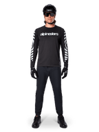 Alpinestars A-Dura Dri Oscar långärmad tröja i Black Reflective, bärs med svart hjälm och solglasögon, med vit logotyp på bröstet och reflekterande grafiska mönster på ärmarna, MTB-utrustning för terrängkörning