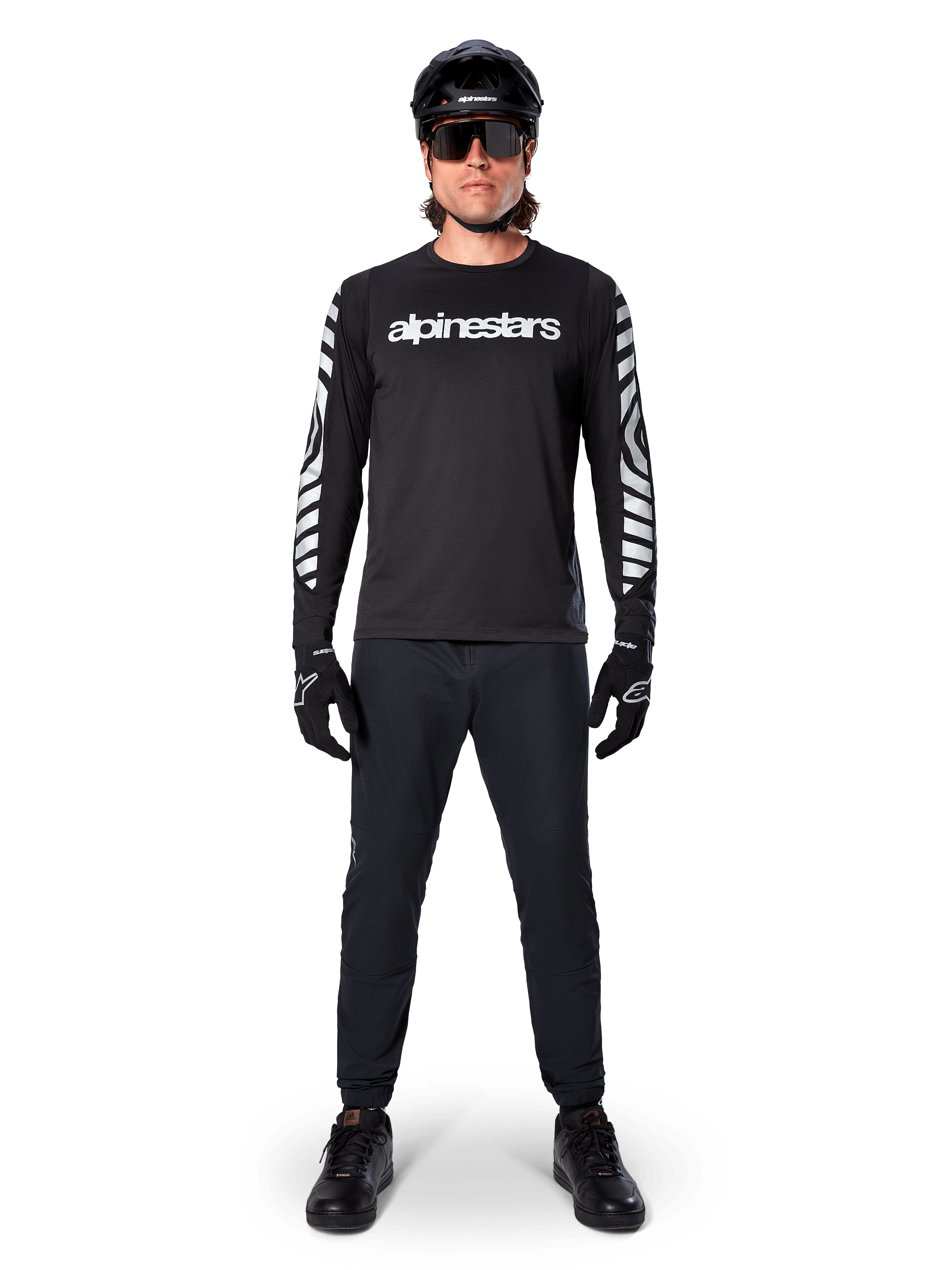 Alpinestars A-Dura Dri Oscar långärmad tröja i Black Reflective, bärs med svart hjälm och solglasögon, med vit logotyp på bröstet och reflekterande grafiska mönster på ärmarna, MTB-utrustning för terrängkörning