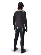 Mountainbike-cyklist som bär Alpinestars A-Dura Dri Oscar långärmad tröja i Black Reflective, sedd bakifrån, kombinerad med svarta tekniska byxor, hjälm och handskar, med reflekterande ränder på axlarna och ett förlängt ryggslut för terrängcykling.