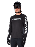Alpinestars A-Dura Dri Oscar långärmad tröja, MTB-tröja, svart med reflekterande detaljer, vit textlogotyp på bröstet och framträdande reflekterande cirkulär grafik på ärmarna, bärs med svart hjälm och solglasögon, tekniskt fukttransporterande material för terrängcykling