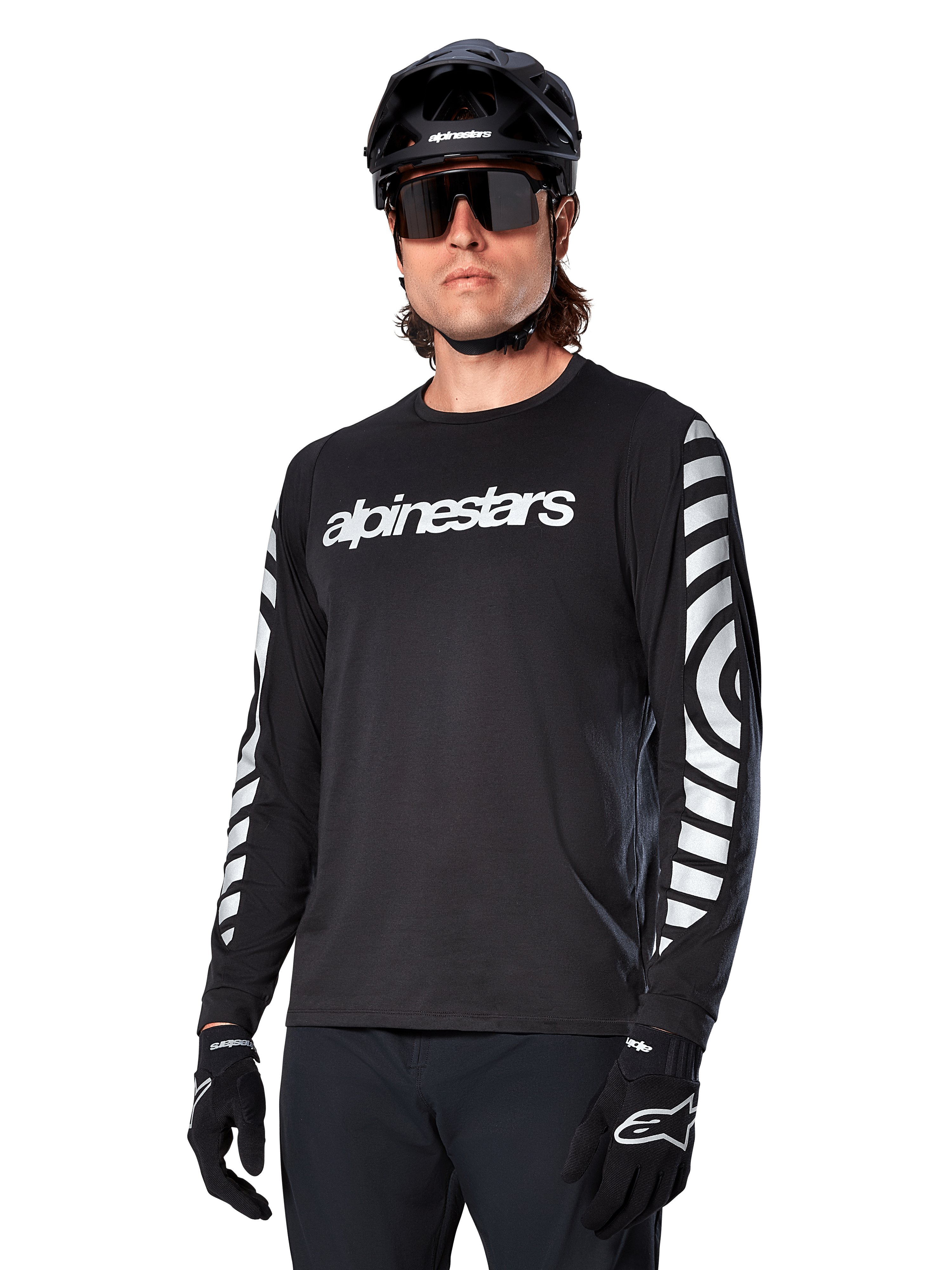 Alpinestars A-Dura Dri Oscar långärmad tröja, MTB-tröja, svart med reflekterande detaljer, vit textlogotyp på bröstet och framträdande reflekterande cirkulär grafik på ärmarna, bärs med svart hjälm och solglasögon, tekniskt fukttransporterande material för terrängcykling