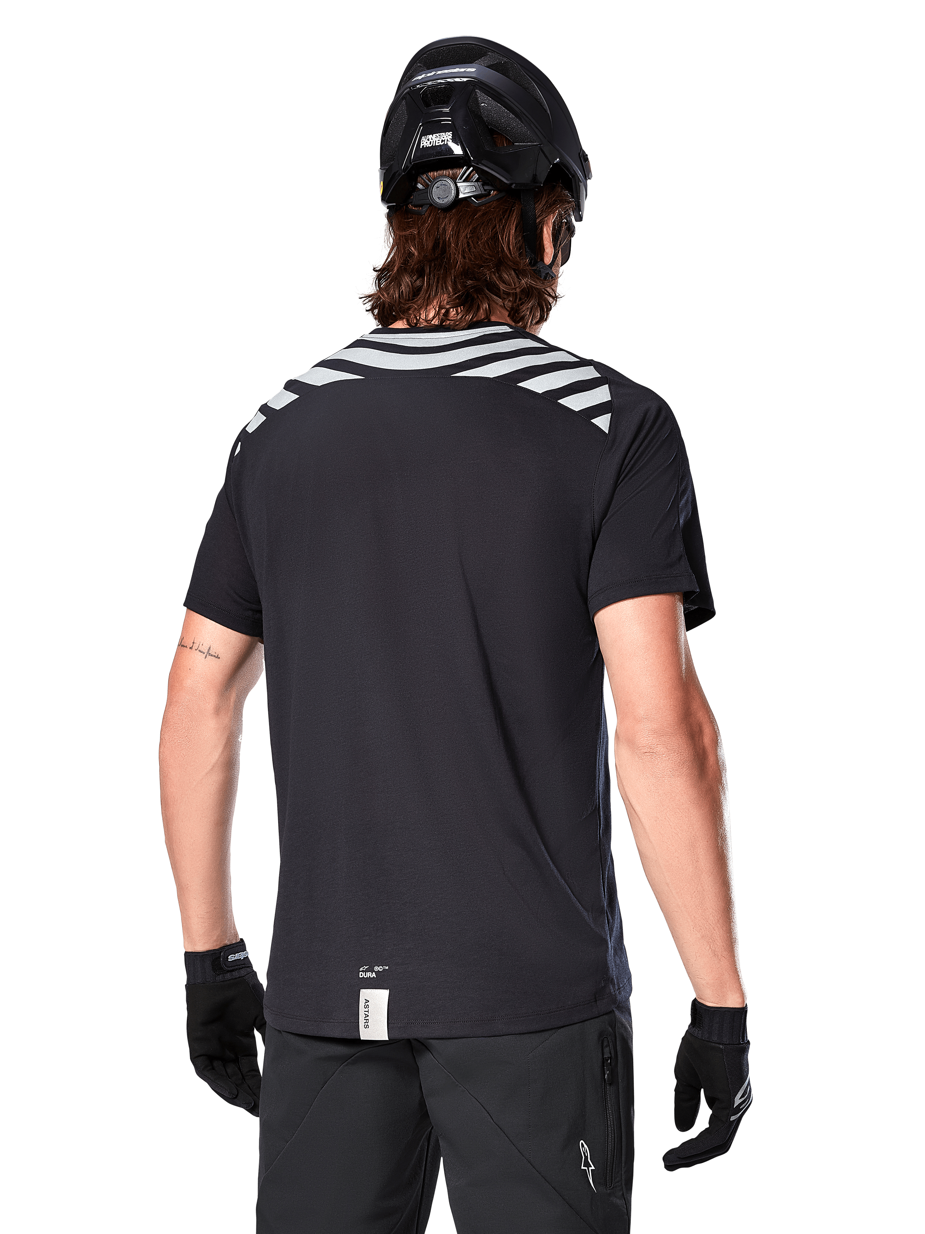 Alpinestars A-Dura Dri Oscar-tröja, kortärmad MTB-tröja, Black Reflective, ryggvy på modell som bär cykelhjälm och handskar, med reflekterande grå axelränder och förlängt ryggslut, fukttransporterande tekniskt material för mountainbike