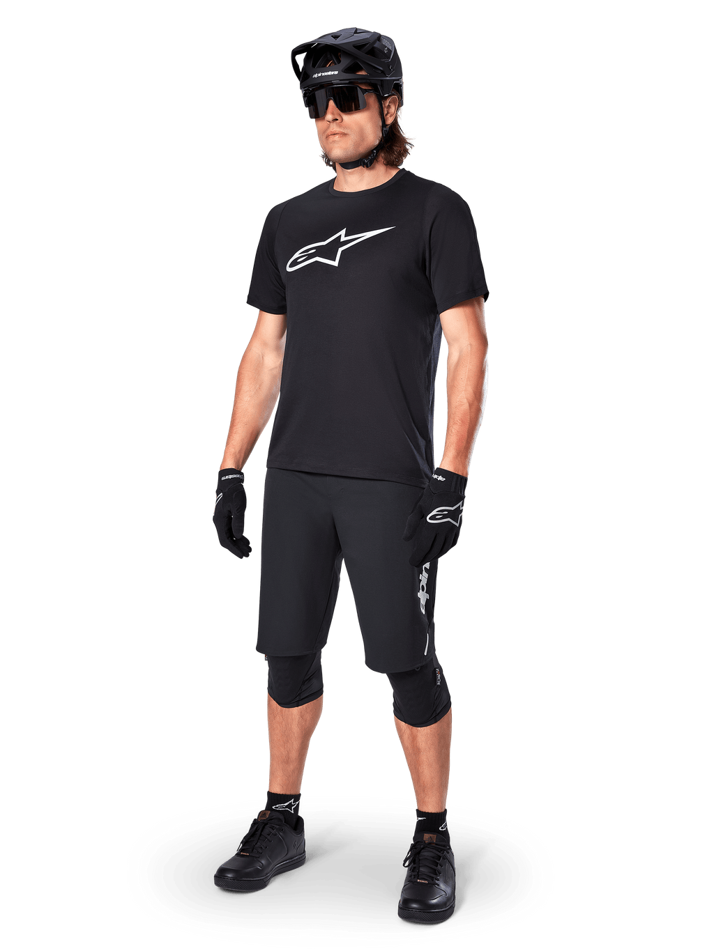 Mountainbike-cyklist som bär Alpinestars A-Dura Dri Oscar kortärmad tröja i Black Reflective, med en stor vit logotyp på bröstet, kombinerat med matchande svarta MTB-shorts, handskar och hjälm, tekniska cykelkläder för terrängprestanda