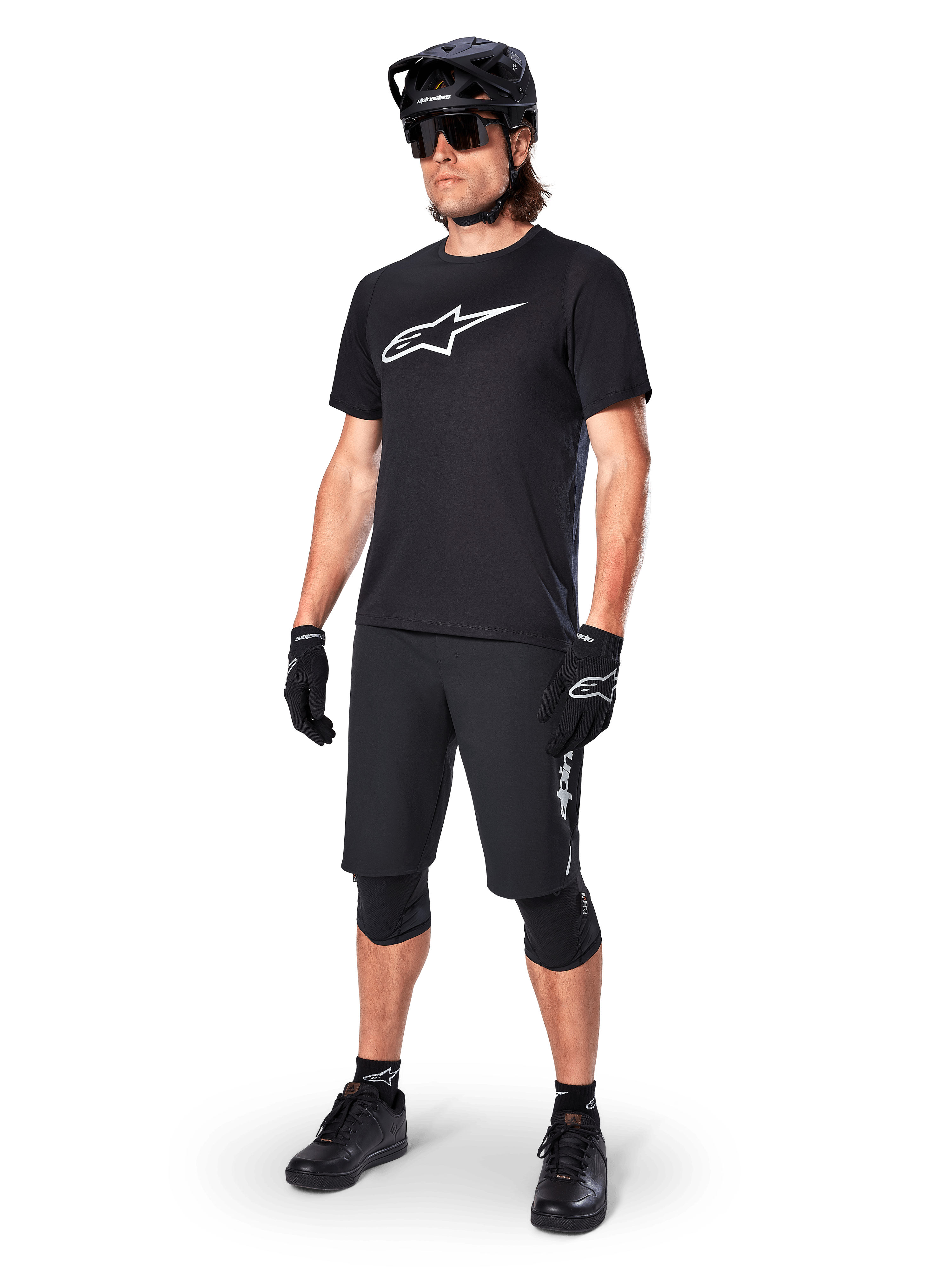 Mountainbike-cyklist som bär Alpinestars A-Dura Dri Oscar kortärmad tröja i Black Reflective, med en stor vit logotyp på bröstet, kombinerat med matchande svarta MTB-shorts, handskar och hjälm, tekniska cykelkläder för terrängprestanda