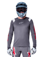 MTB-cyklist iförd Alpinestars A-Supra Astar långärmad tröja, mörkgrå med röd grafik på ärmarna och vita detaljer på axlarna, matchande grå byxor med röda stjärnlogotyper, blå fullfacehjälm och goggles, koordinerad cykelutrustning för terrängkörning