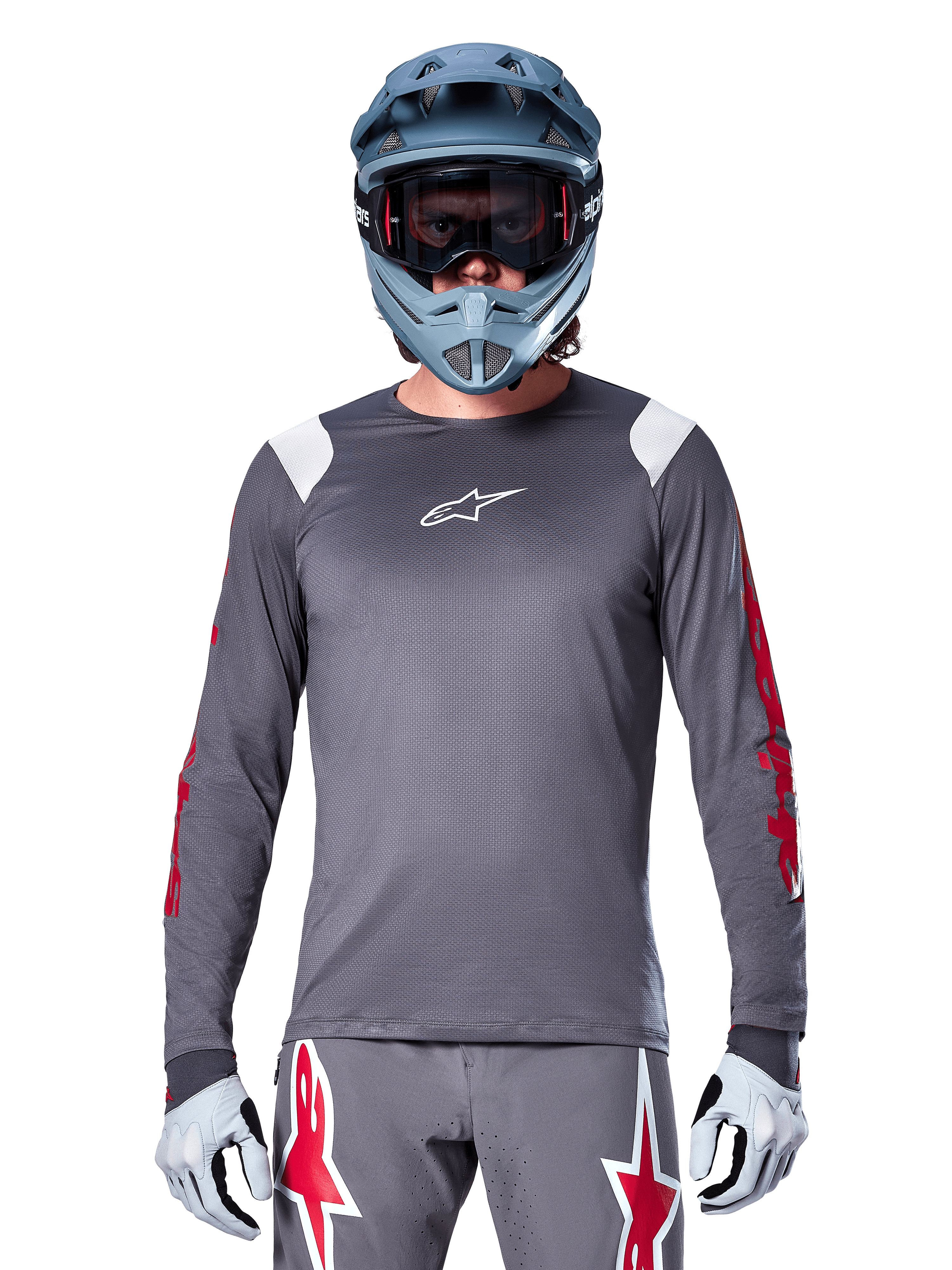 MTB-cyklist iförd Alpinestars A-Supra Astar långärmad tröja, mörkgrå med röd grafik på ärmarna och vita detaljer på axlarna, matchande grå byxor med röda stjärnlogotyper, blå fullfacehjälm och goggles, koordinerad cykelutrustning för terrängkörning
