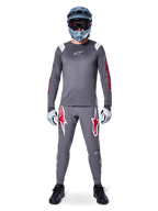 MTB-cyklist i Alpinestars A-Supra Astar långärmad tröja, mörkgrå med röda detaljer och vit bröstlogotyp, matchande grå byxor med stora röda stjärngrafiker, blå fullfacehjälm med goggles, ljusgrå handskar och svarta skor, professionell mountainbike-utrustning