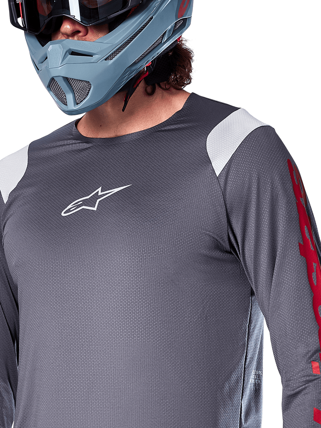 Alpinestars A-Supra Astar långärmad tröja, mörkgrå med vita axelpaneler och röd grafik på ärmarna, bärs med en ljus blågrå fullfacehjälm, funktionskläder för mountainbike