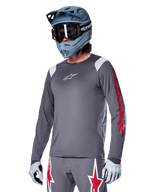 Alpinestars A-Supra Astar långärmad tröja, MTB-tröja, mörkgrå med röda och vita detaljer, prestandapassform, bärs med matchande grå byxor med röd och vit stjärngrafik, komplett outfit för terrängcykling med fullface-hjälm och handskar