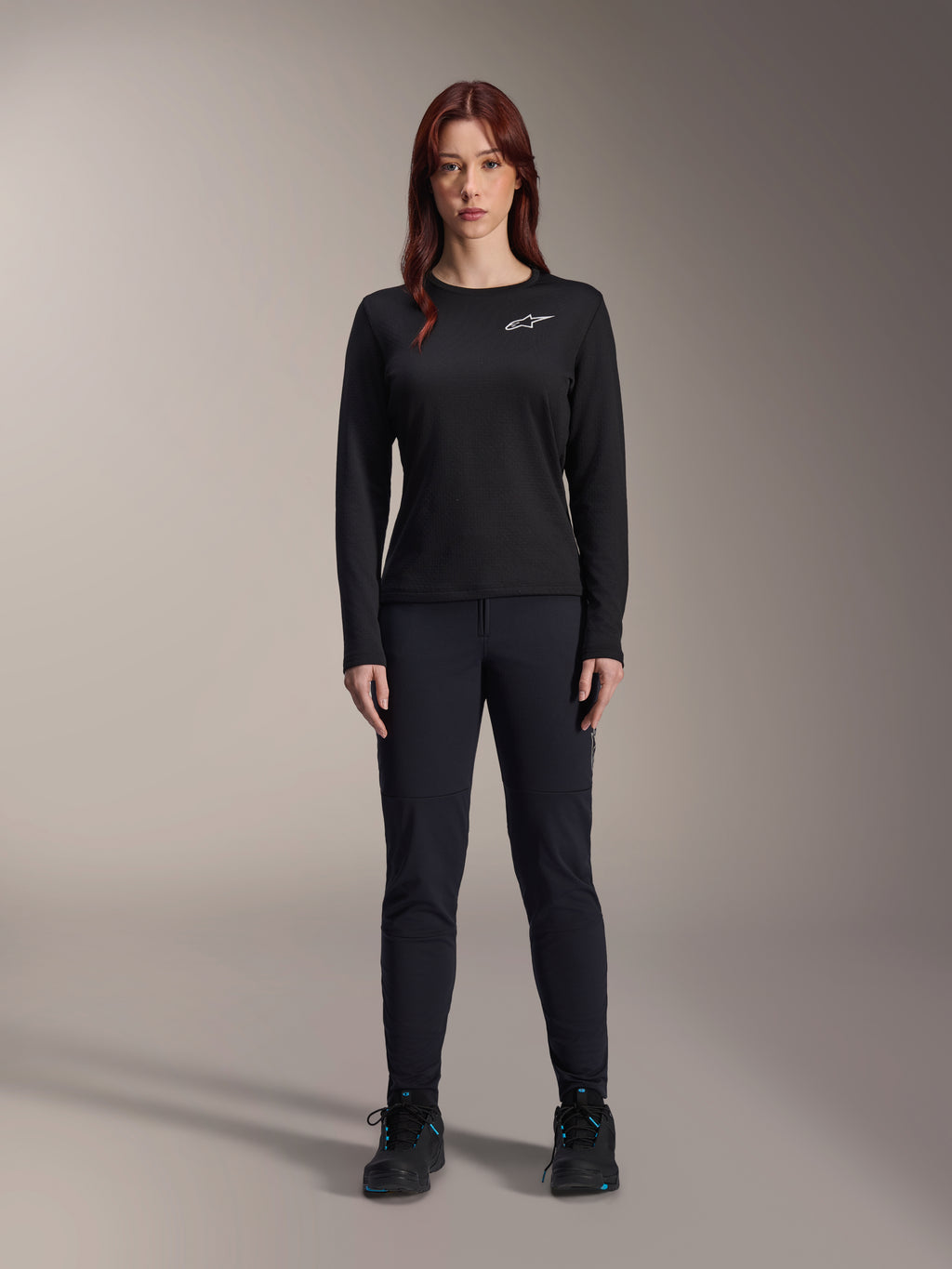 Alpinestars Stella A-Dura Thermal-tröja, långärmad mountainbike-tröja för damer i svart, med en vit logotyp på bröstet, bärs med matchande svart utrustning och cykelskor, studioporträtt.