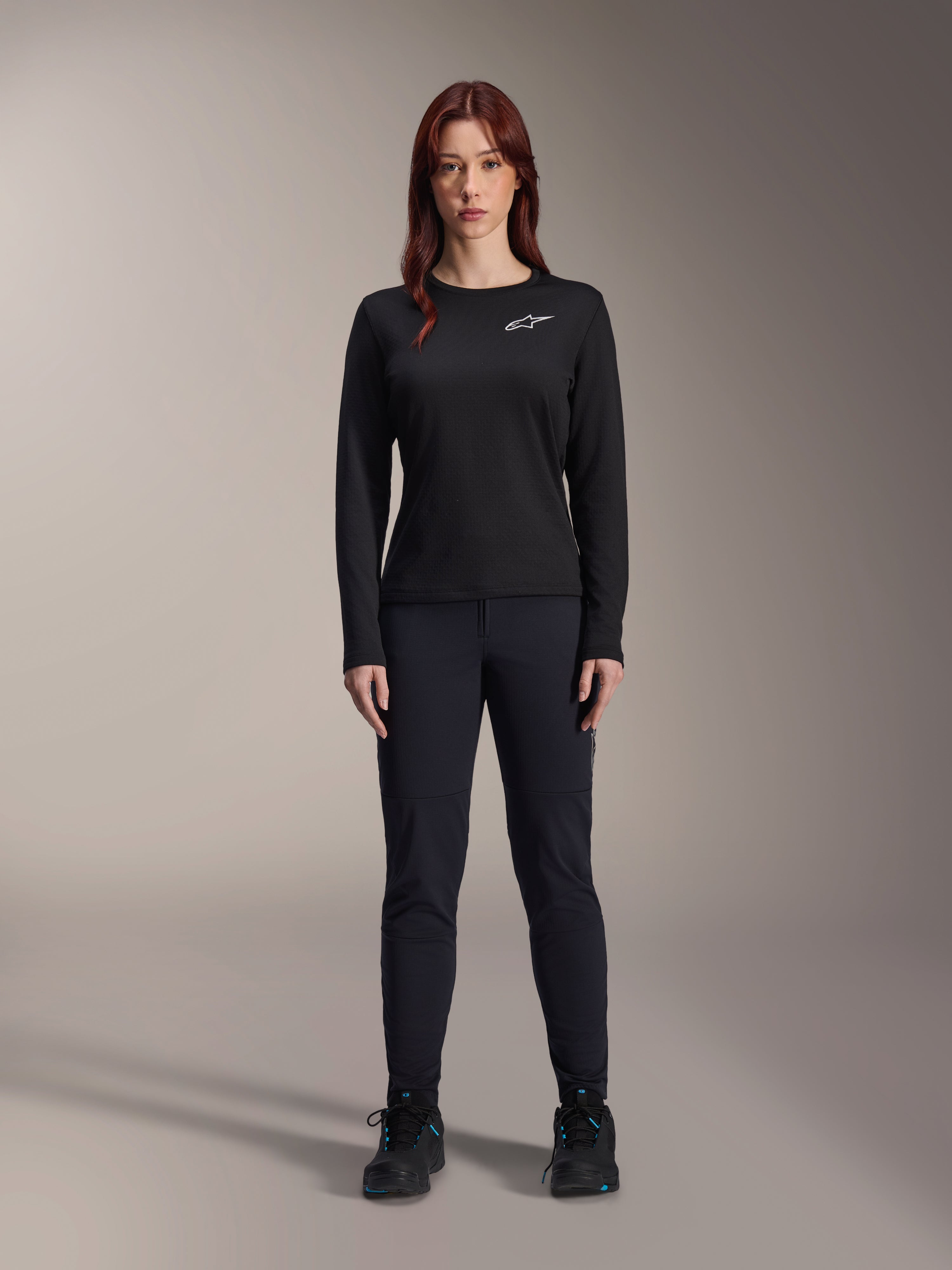Alpinestars Stella A-Dura Thermal-tröja, långärmad mountainbike-tröja för damer i svart, med en vit logotyp på bröstet, bärs med matchande svart utrustning och cykelskor, studioporträtt.
