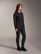 Kvinna som bär Alpinestars Stella A-Dura Thermal Jersey, långärmad svart MTB-tröja med vit logotyp på bröstet, stylad med matchande svarta byxor och sportskor, studioporträtt för funktionella cykelkläder