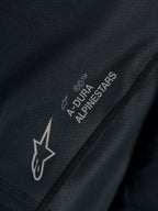 Svart Stella A-Dura Ride-tröja, närbild på tekniskt jacquardtyg med A-DURA ALPINESTARS och Astars-logotyper.