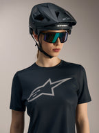 Stella A-Dura Ride kortärmad tröja för dam i svart, stor grå bröstlogotyp, buren med MTB-hjälm och solglasögon.