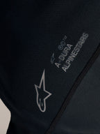 Närbild på svart Stella A-Dura Ride-tröja med vit Alpinestars-logotyp och A-DURA-märkning på jacquardvävt tyg.