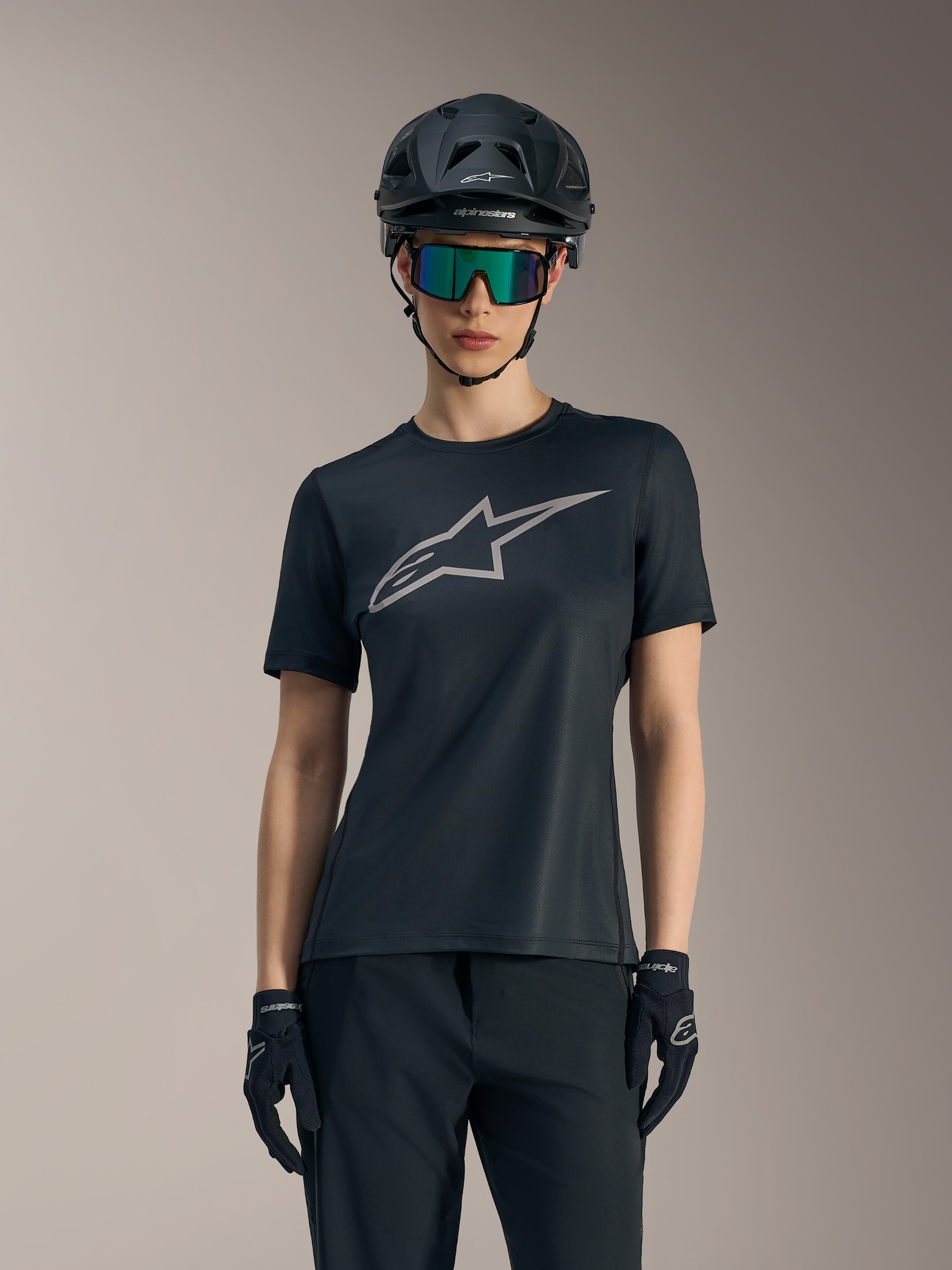 Svart Stella A-Dura Ride-tröja för damer med grå bröstlogotyp, stylad med mountainbikehjälm och goggles.