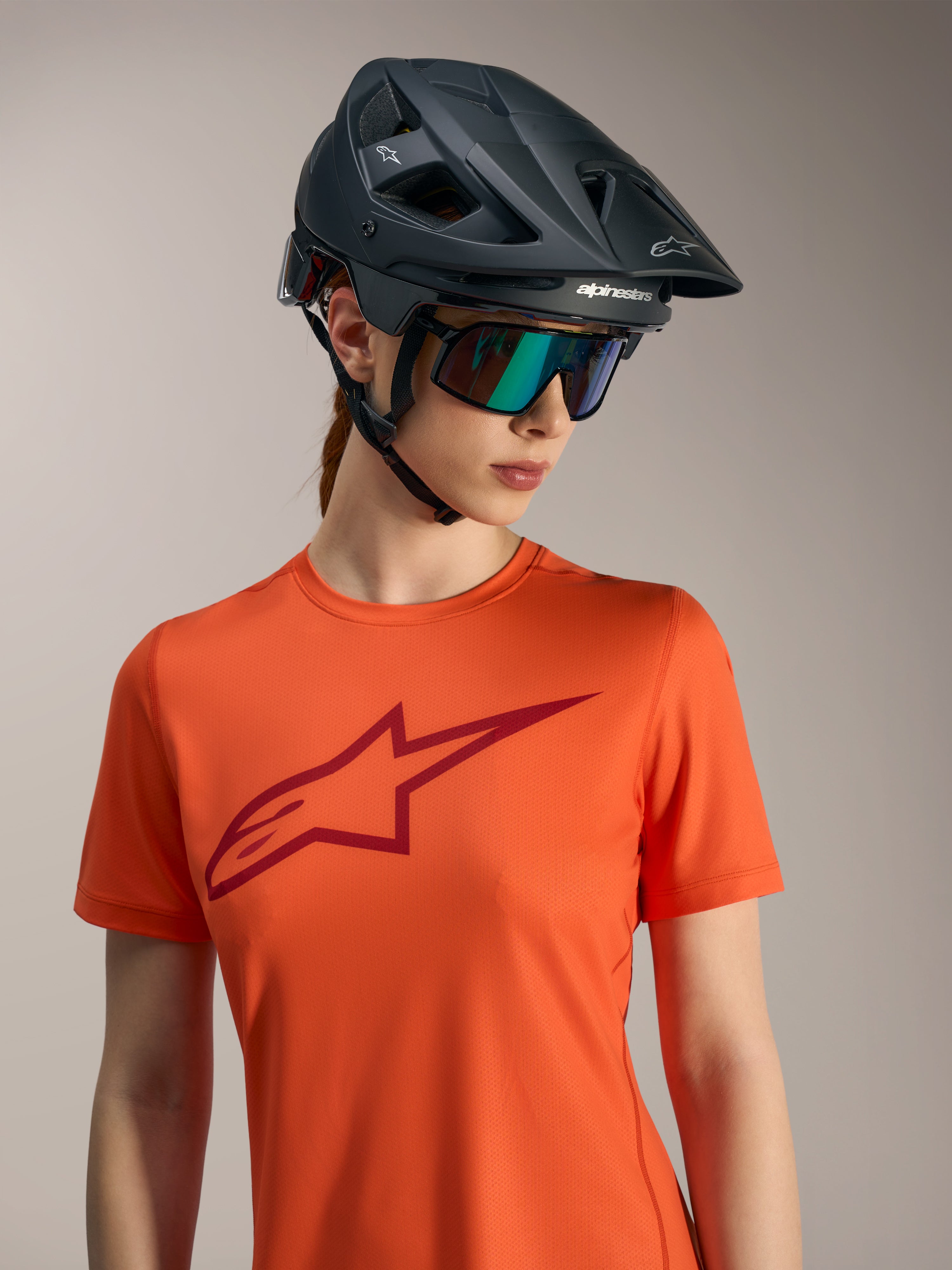Orange Alpinestars Stella A-Dura Ride kortärmad tröja med röd logotyp, svart MTB-hjälm och iriserande solglasögon.