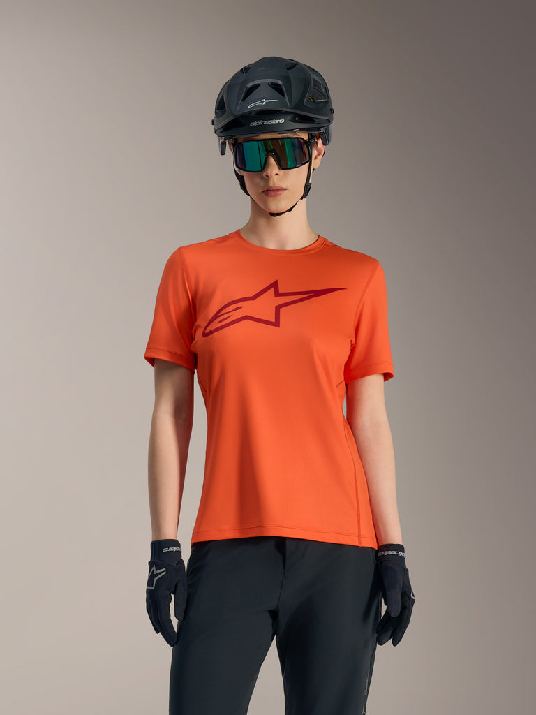 Orange Women's Stella A-Dura Ride short sleeve jersey with red logo, styled with black MTB helmet and sunglasses.