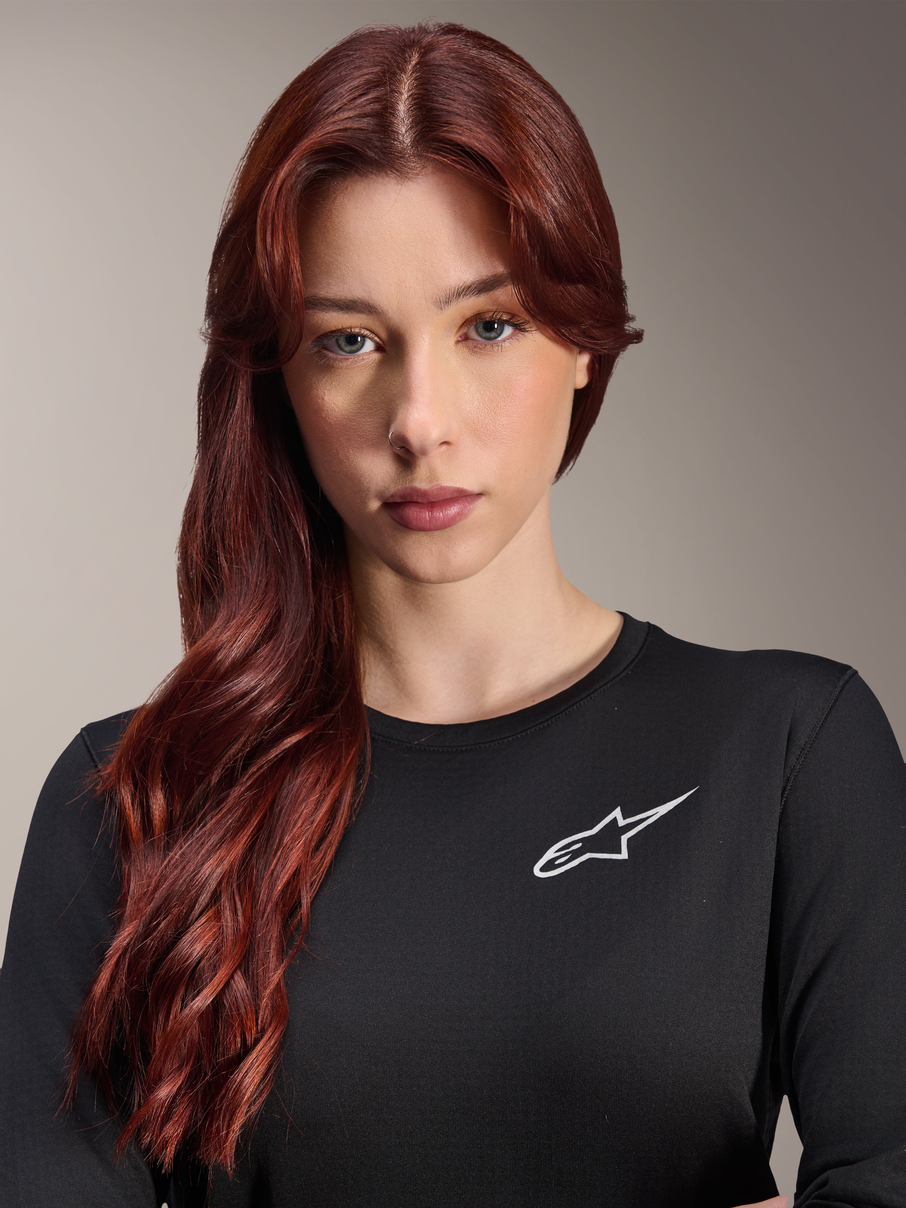Alpinestars Stella A-Dura Thermal-tröja, långärmad MTB-tröja för dam, svart med vit Alpinestars-logotyp på bröstet, närbildsporträtt av en kvinna med långt rött hår, cykelkläder för svalt väder