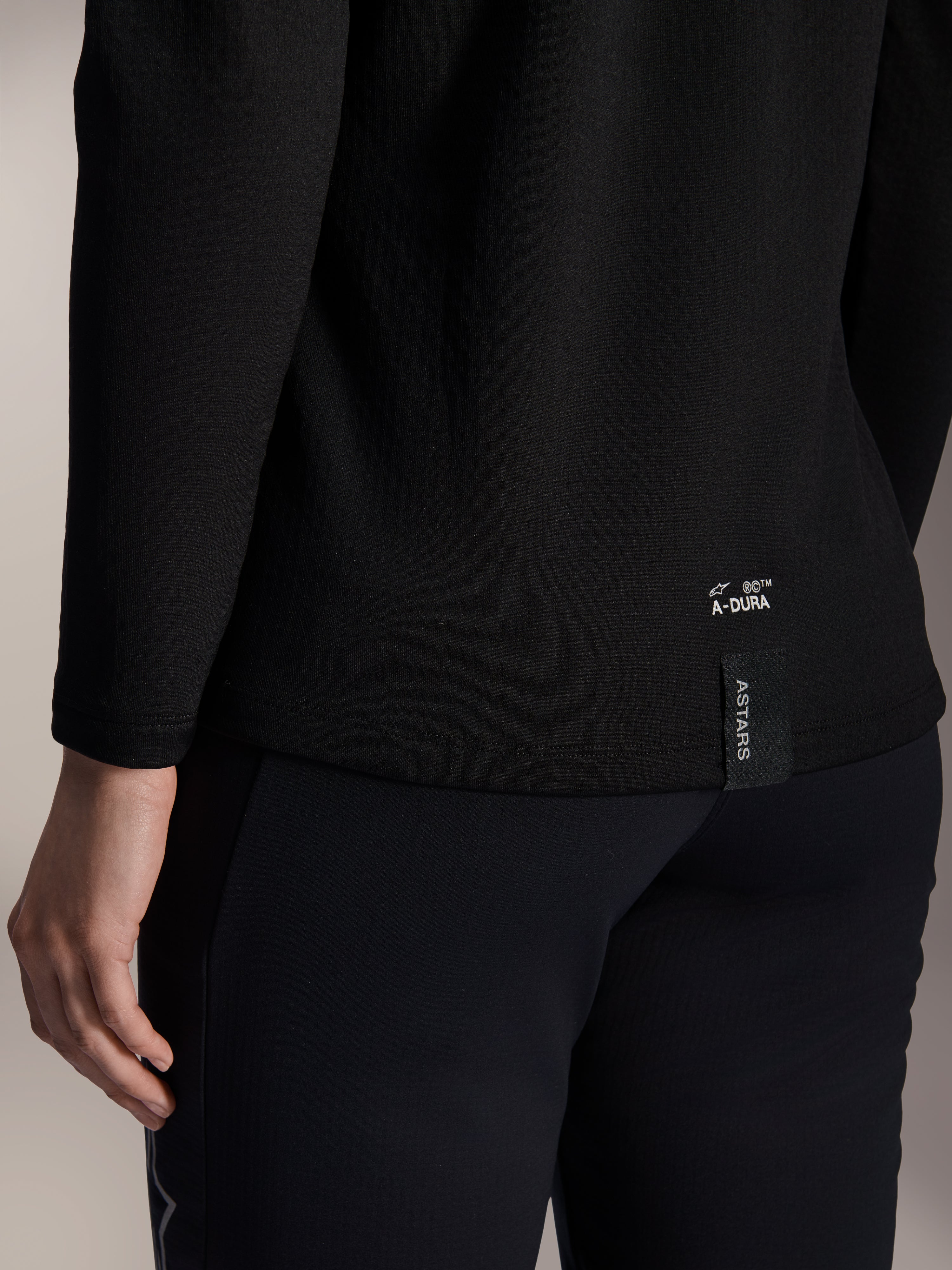 Alpinestars Stella A-Dura Thermal-tröja för dam, svart termotröja för MTB, närbild på nedre fållen baktill med vit A-DURA-logotyp och vertikal ASTARS-logga, designad för mountainbikecykling i kallt väder