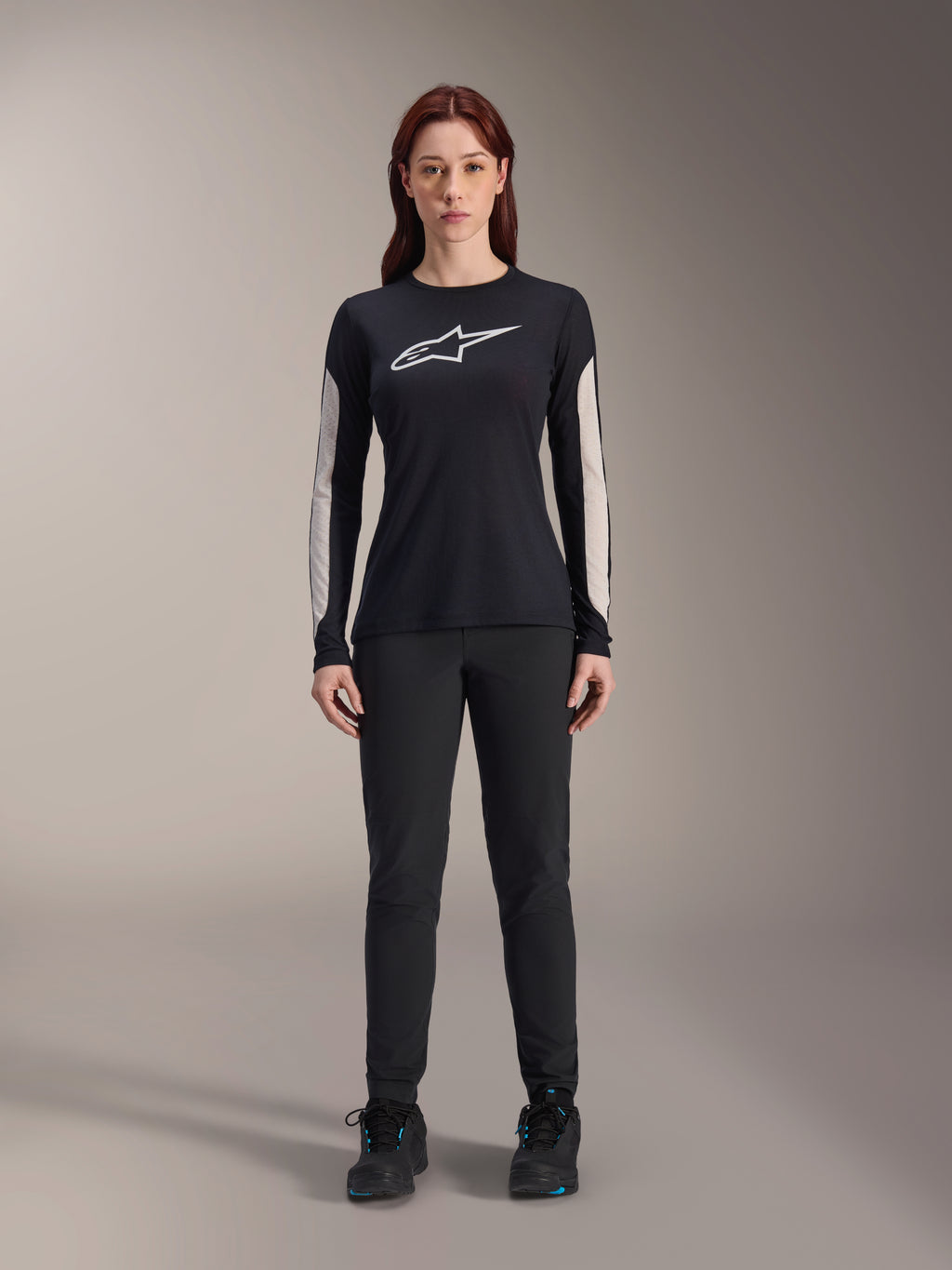 Kvinna i Alpinestars Stella A-Dura Dri Astar långärmad tröja, svart med vit logotyp på bröstet och ljusa meshpaneler på ärmarna, kombinerat med svarta byxor och svarta skor, tekniska mountainbikekläder