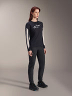 Kvinna i Alpinestars MTB-utrustning, svart Stella A-Dura Elite-tröja med vit logotyp på bröstet och paneler på ärmarna, svarta Stella A-Dura-byxor, svarta cykelskor med blå detaljer, komplett outfit för mountainbike