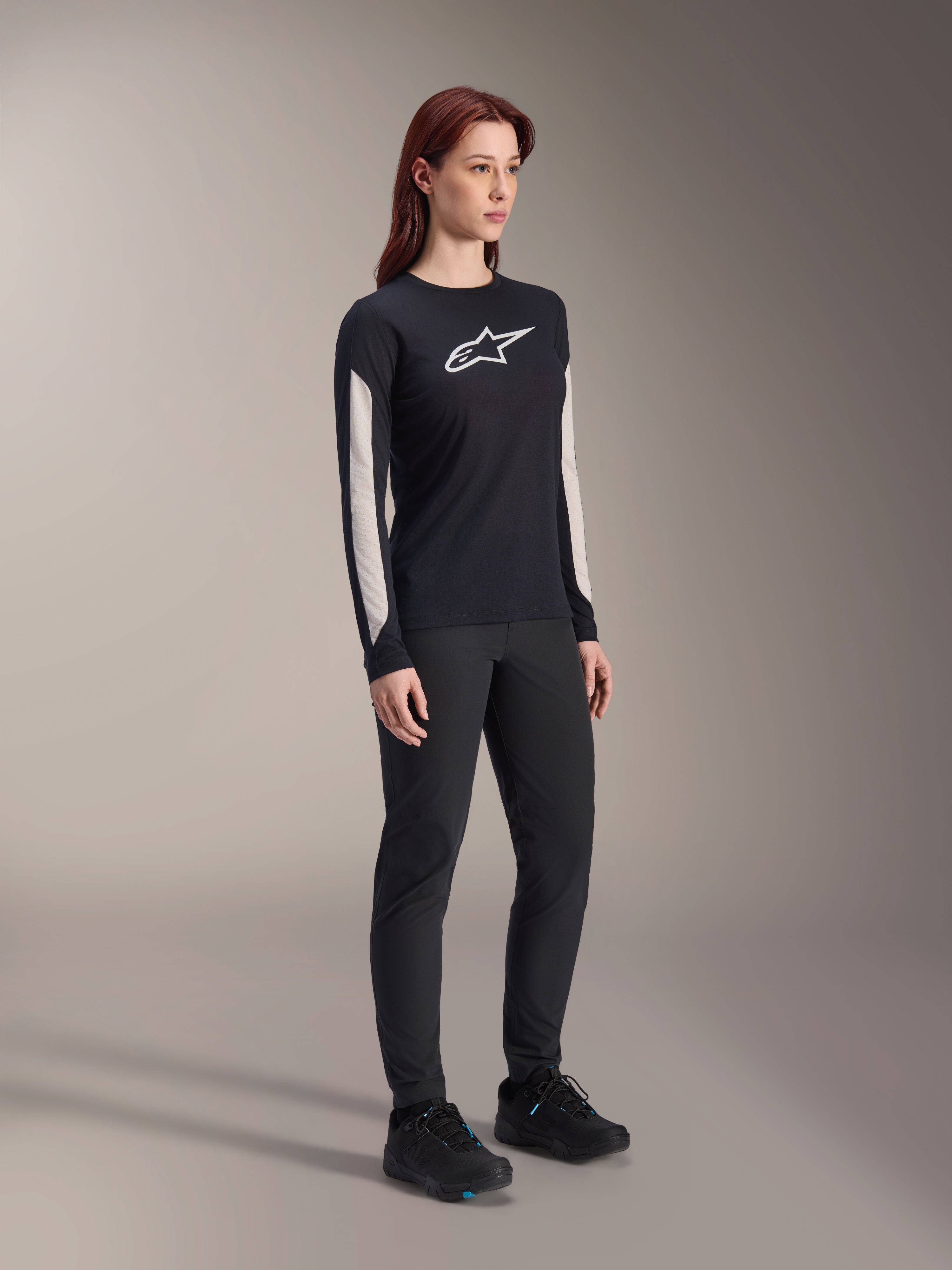 Kvinna i Alpinestars MTB-utrustning, svart Stella A-Dura Elite-tröja med vit logotyp på bröstet och paneler på ärmarna, svarta Stella A-Dura-byxor, svarta cykelskor med blå detaljer, komplett outfit för mountainbike