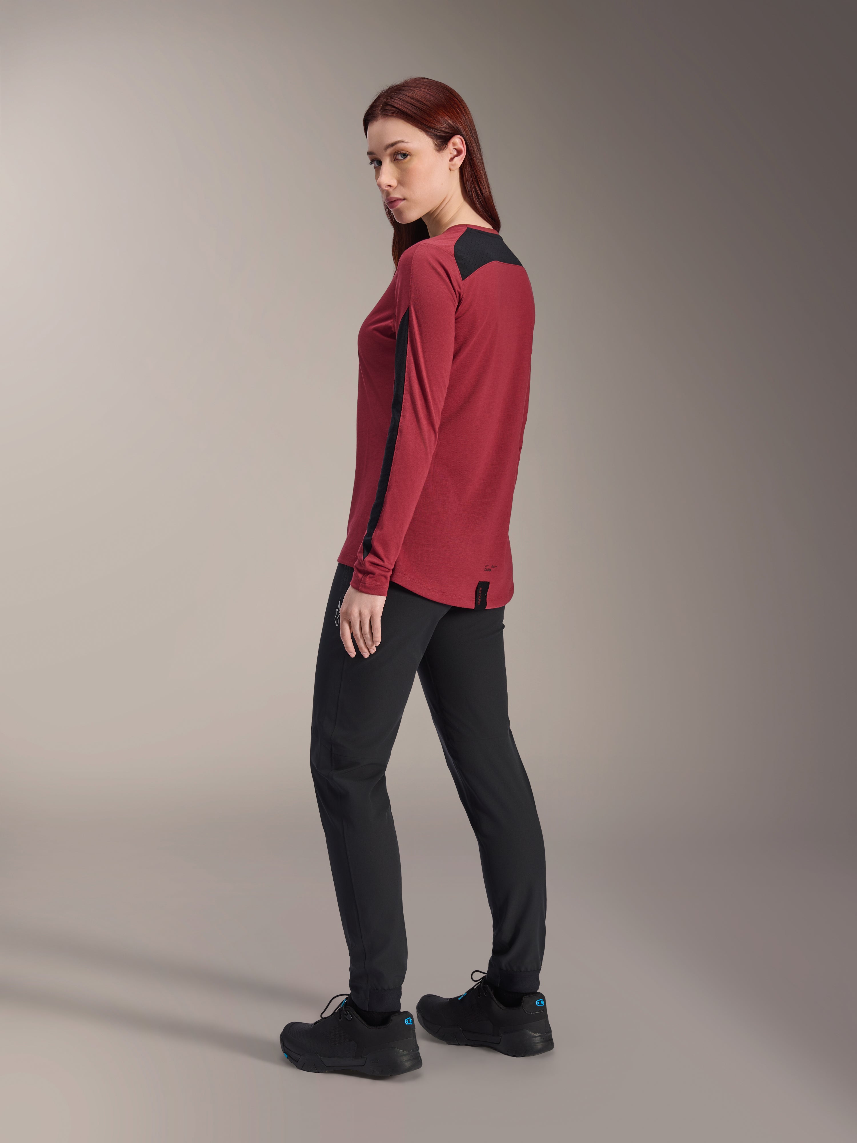 Alpinestars Stella A-Dura Dri Astar långärmad tröja för dam, vinröd och svart, bärs med svarta MTB-byxor och svarta skor, profilvy bakifrån, återvunnet drirelease-tyg med meshpaneler, tekniska mountainbikekläder