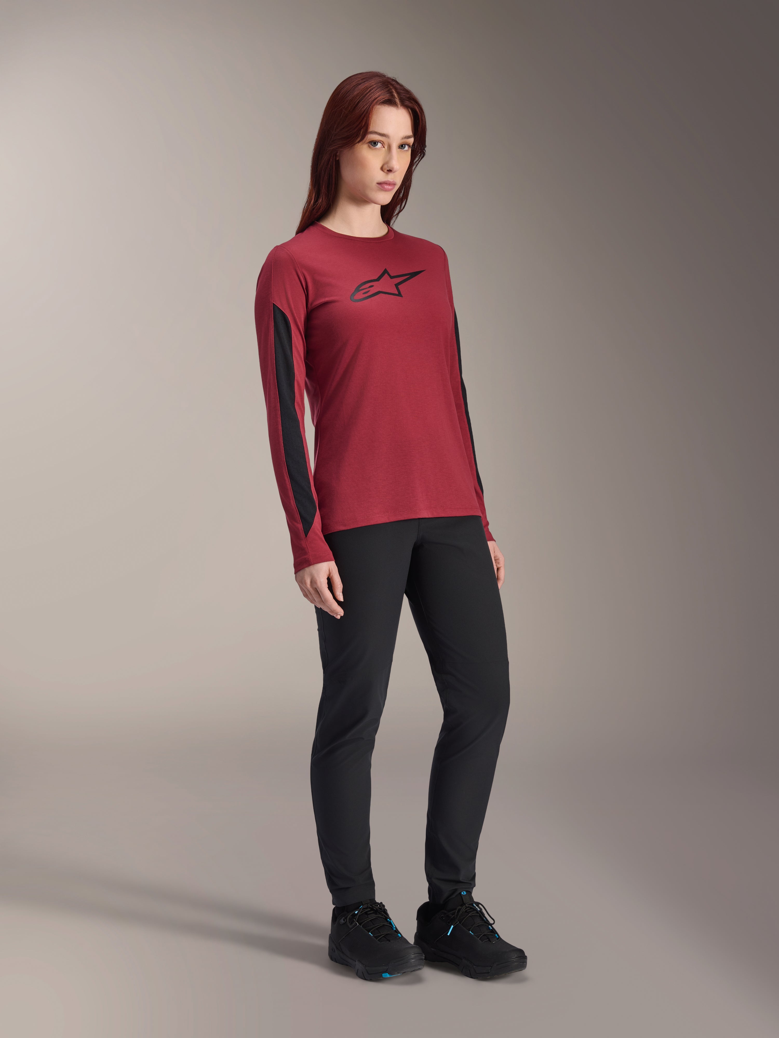 Alpinestars Stella A-Dura Dri Astar långärmad tröja för dam, burgundyröd med svart logotyp på bröstet och svarta meshpaneler på ärmarna, buren med svarta tekniska byxor och svarta cykelskor, högpresterande mountainbike-kläder för dam