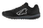 Alpinestars Meta Trail-skor, prestationslöparsko, svarta och mörkgrå, sidoprofil med stor vit Astars-logotyp, mörkgrå mellansula, räfflad oljebeständig gummisula, designad för komfort i paddocken och för motorsportsteam